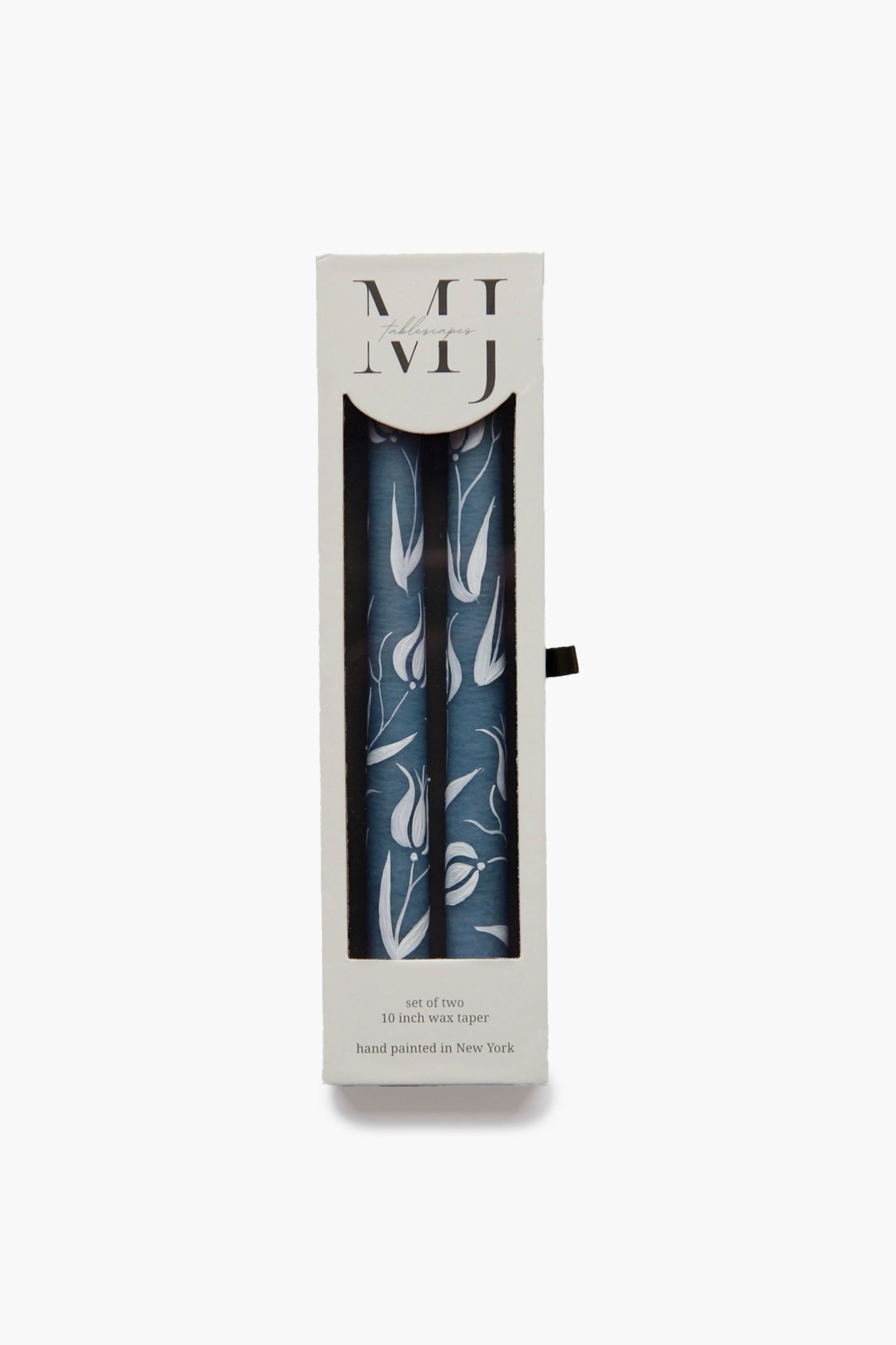 A box of two blue tulip candles with a white floral pattern from MJ Tablescapes, partially visible through a clear window. The packaging features printed text and MJ Tablescapes branding.