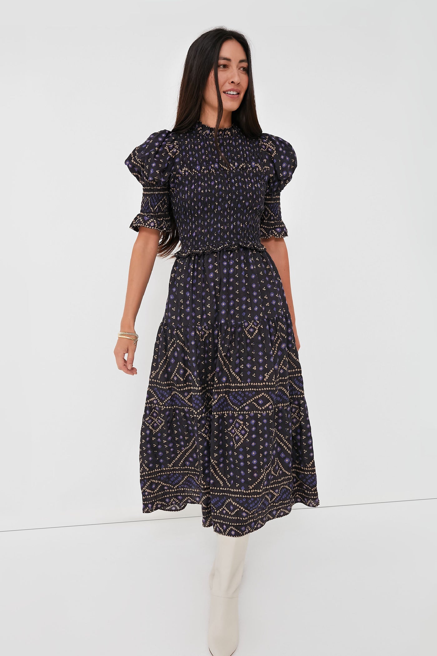 A woman wearing a Sea New York Delphine Pucker Dress in blue, featuring a smocked bodice and short ruffled sleeves, paired with white knee-high boots.