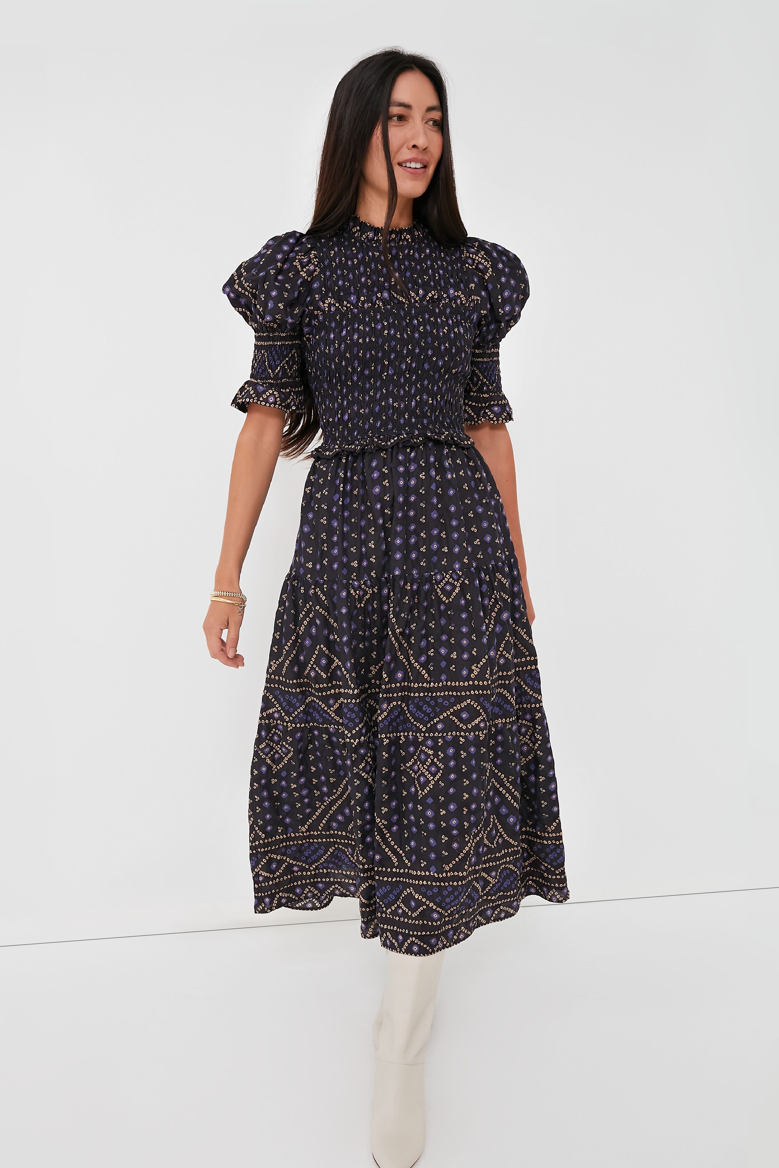 A woman wearing a Sea New York Delphine Pucker Dress in blue, featuring a smocked bodice and short ruffled sleeves, paired with white knee-high boots.