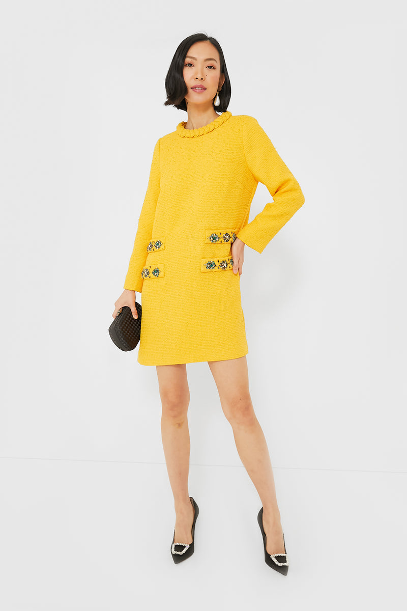 A woman stands confidently in a Tuckernuck yellow textured tweed Jackie Dress with decorative buttons, styled with black heels and a small black clutch.