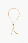 A gold adjustable necklace from Petit Moments, a woman-owned Los Angeles brand, features a round sliding clasp and two dangling ends, each with a small circular charm.