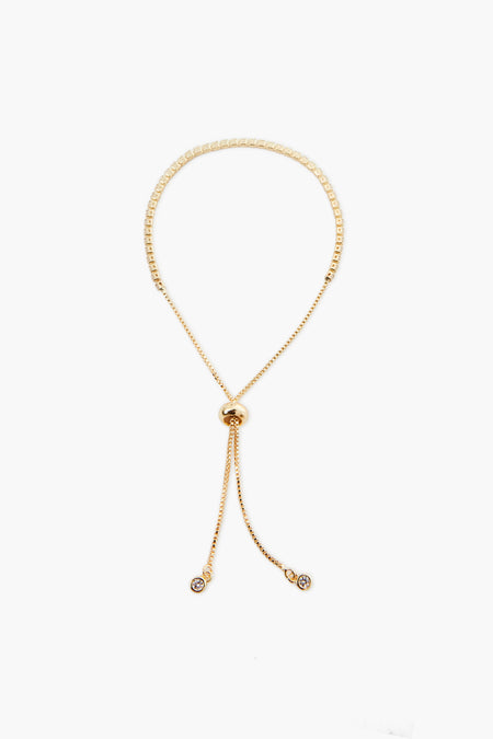 A gold adjustable necklace from Petit Moments, a woman-owned Los Angeles brand, features a round sliding clasp and two dangling ends, each with a small circular charm.