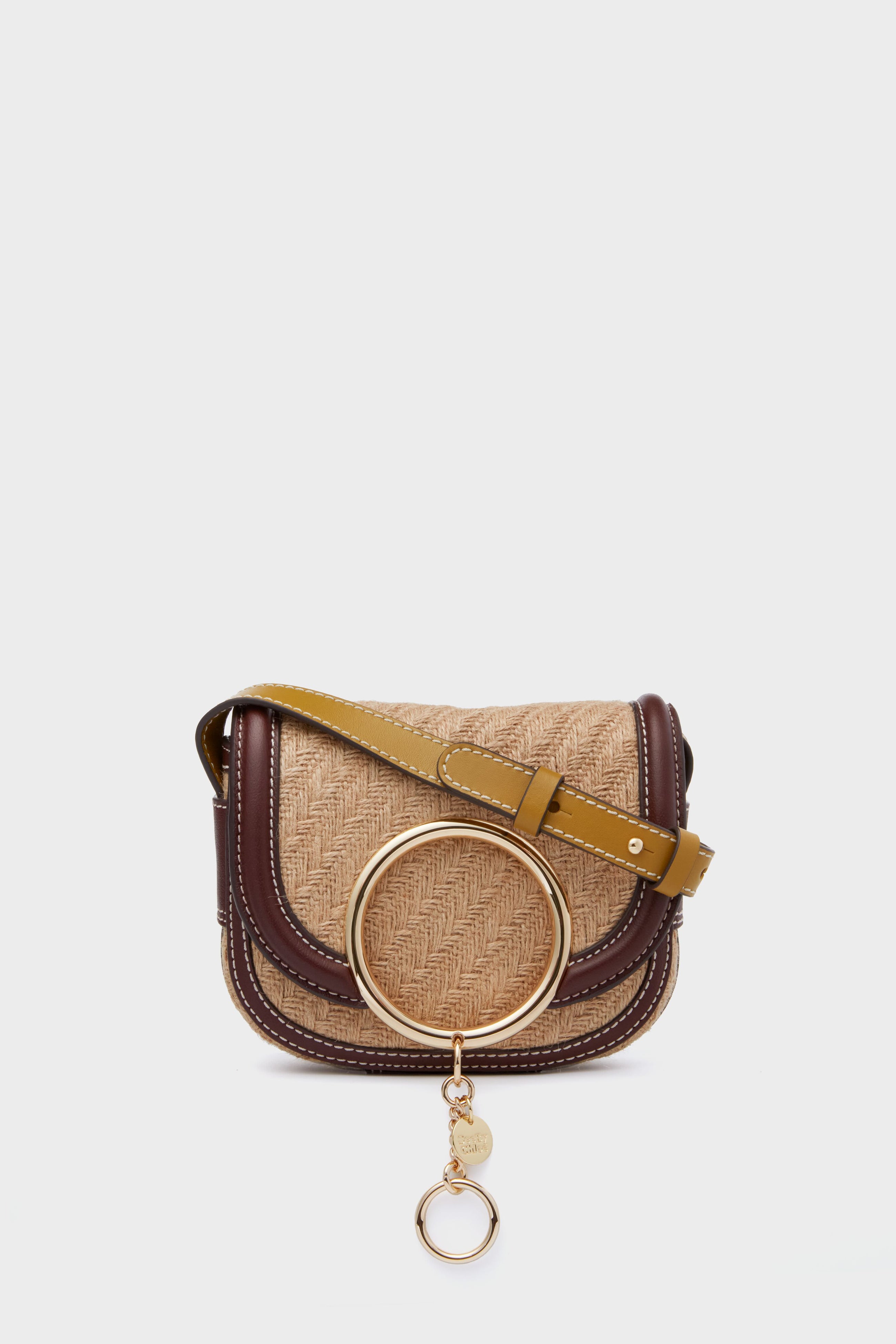 The See by Chloe small jute crossbody bag features a woven straw texture, brown leather trim, yellow strap, and a large gold ring detail on the front.