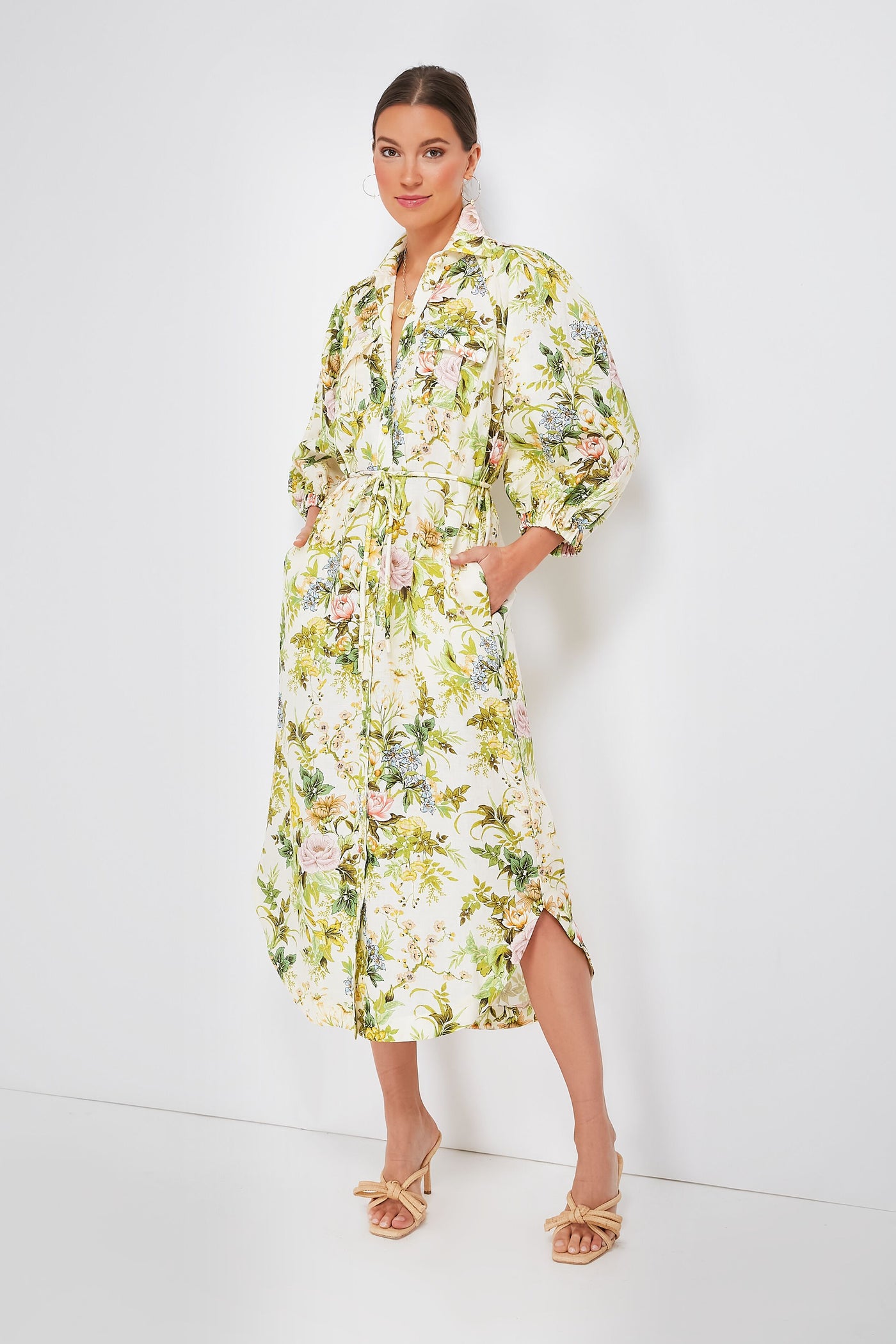 A woman wears a long sleeve Alemais floral shirtdress with a tie waist, styled with beige heeled sandals.