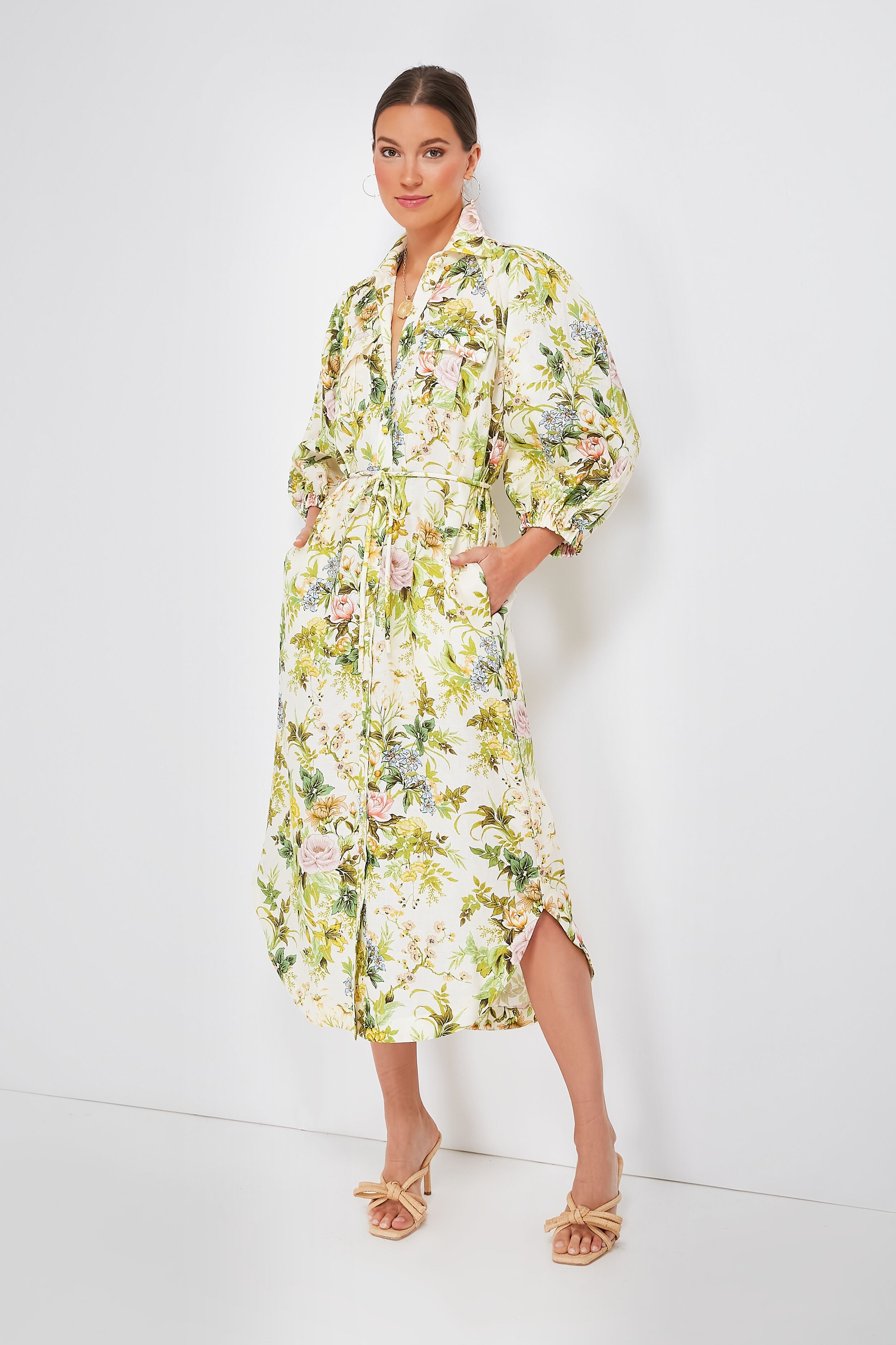 A woman wears a long sleeve Alemais floral shirtdress with a tie waist, styled with beige heeled sandals.