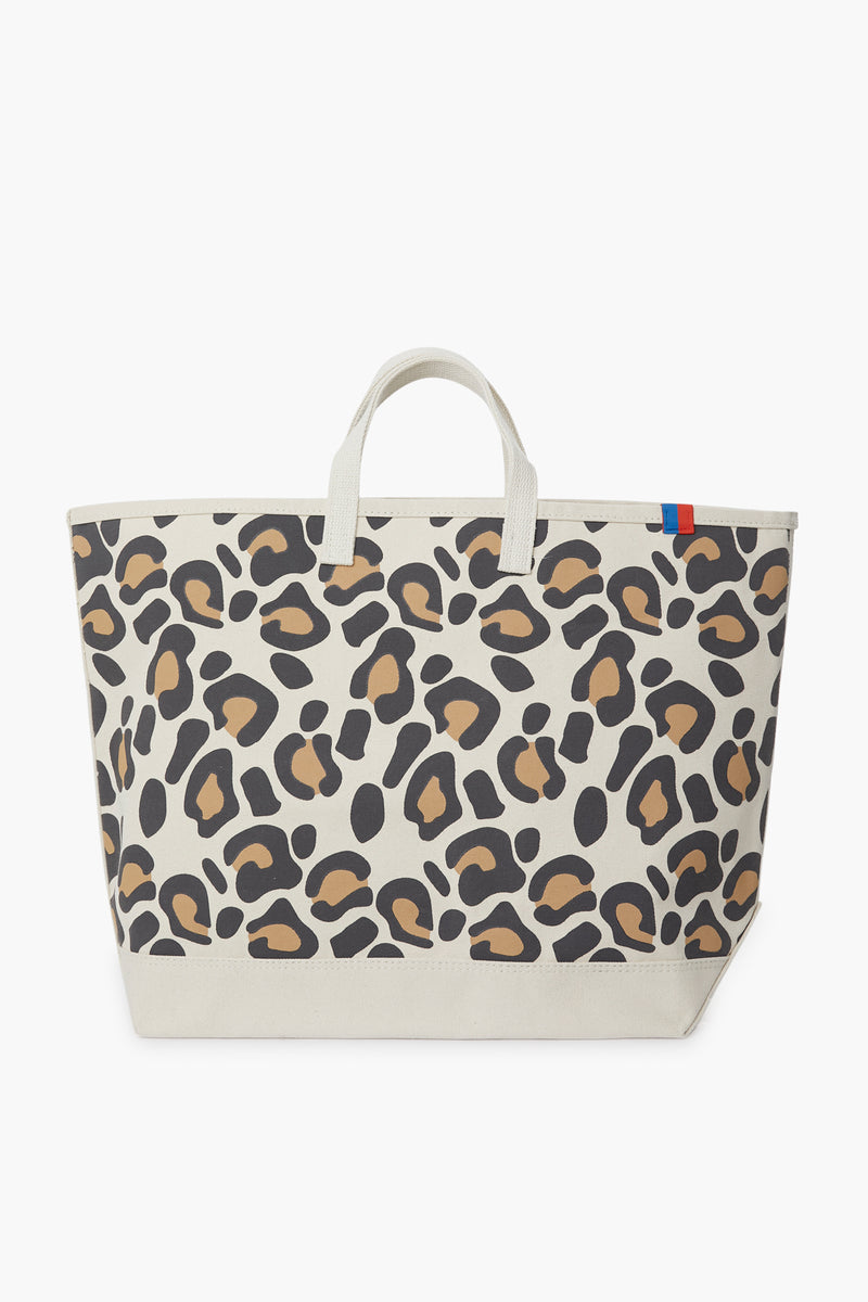 The KULE Large Leopard Tote features short handles, a beige, brown, and black print, and a small blue and red tab on the upper edge—perfect as a stylish daily carry-all.