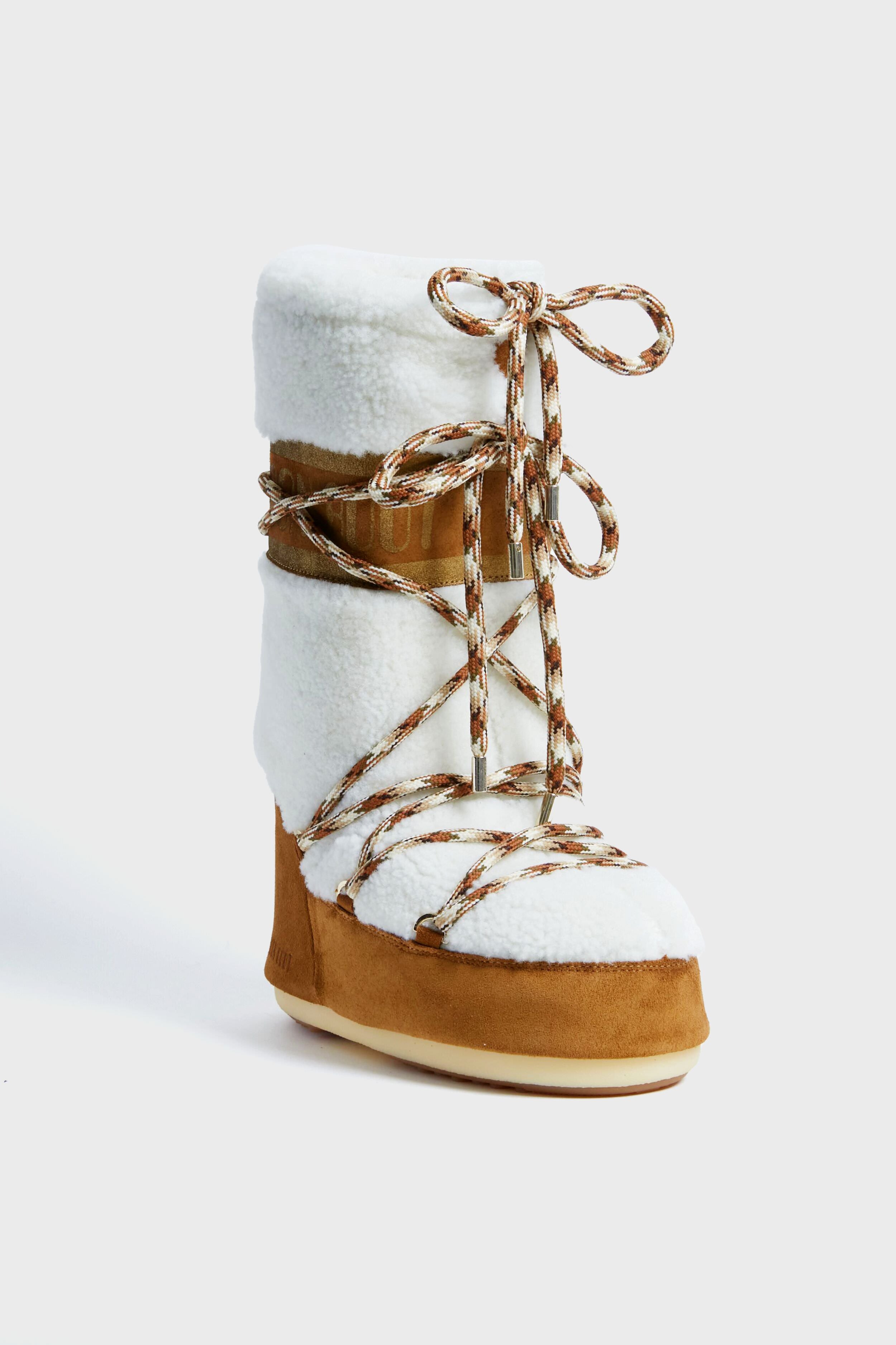 A single Moon Boot après-ski boot featuring a white fleece upper, tan suede lower section, and brown-and-white patterned laces crisscrossing up the front.