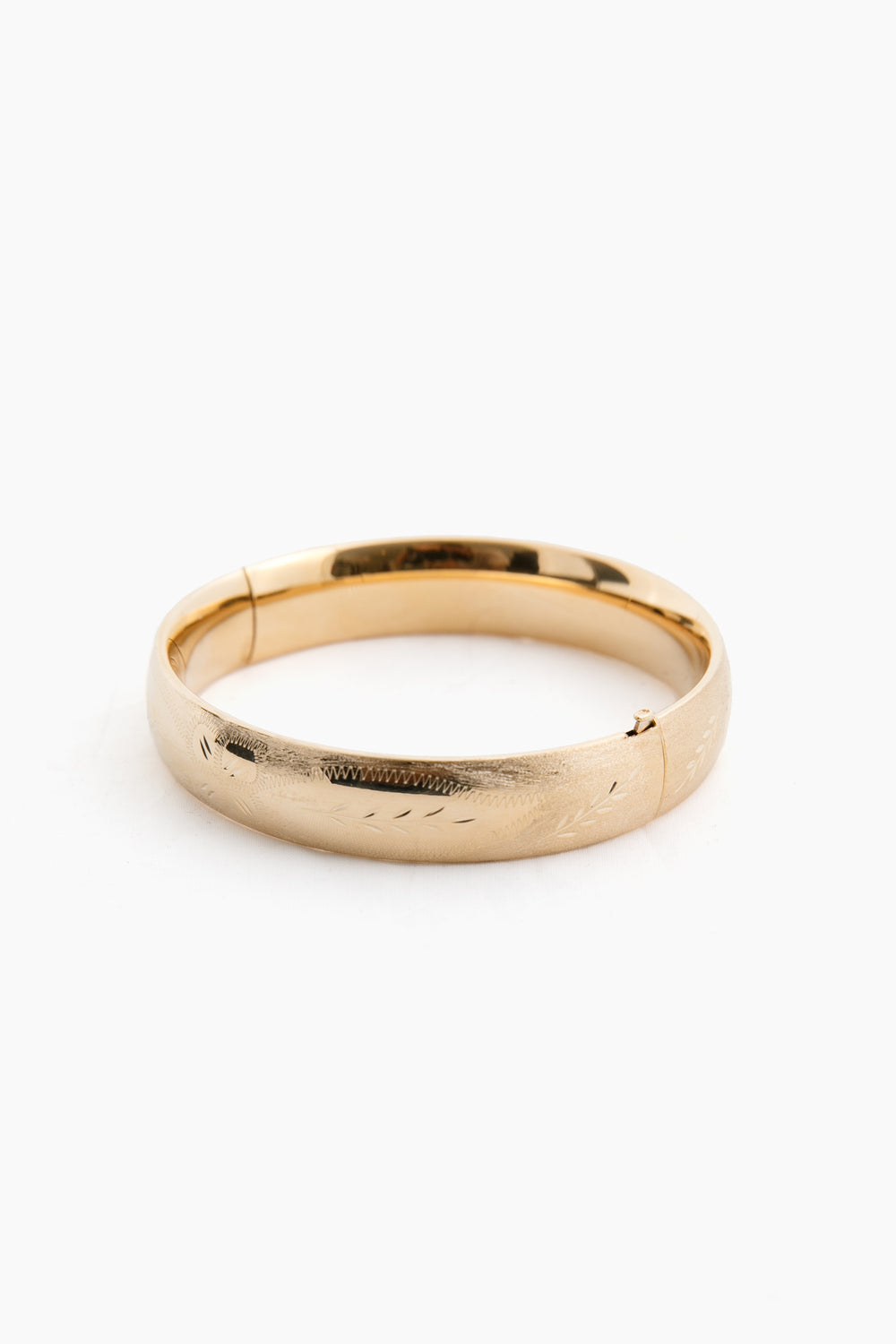 The Tuckernuck Fine Jewelry yellow gold bangle bracelet features a hinged clasp and a subtle engraved pattern, echoing the timeless elegance of classic 14K gold bangles.