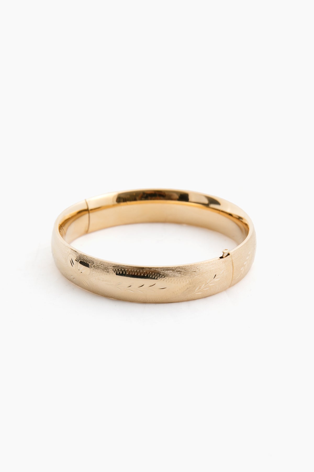 The Tuckernuck Fine Jewelry yellow gold bangle bracelet features a hinged clasp and a subtle engraved pattern, echoing the timeless elegance of classic 14K gold bangles.