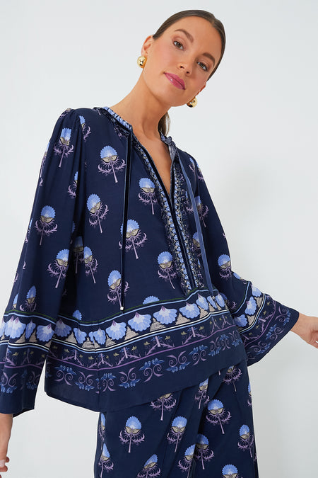 A woman wears the Lug Von Siga Dark Blue Tess Top—100% linen with floral patterns and long sleeves—styled as a matching set and paired with gold earrings.