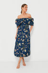 Woman in a Sea New York off-the-shoulder Navy Julian Embroidery Dress with puffed sleeves, gold hoop earrings, and strappy sandals.