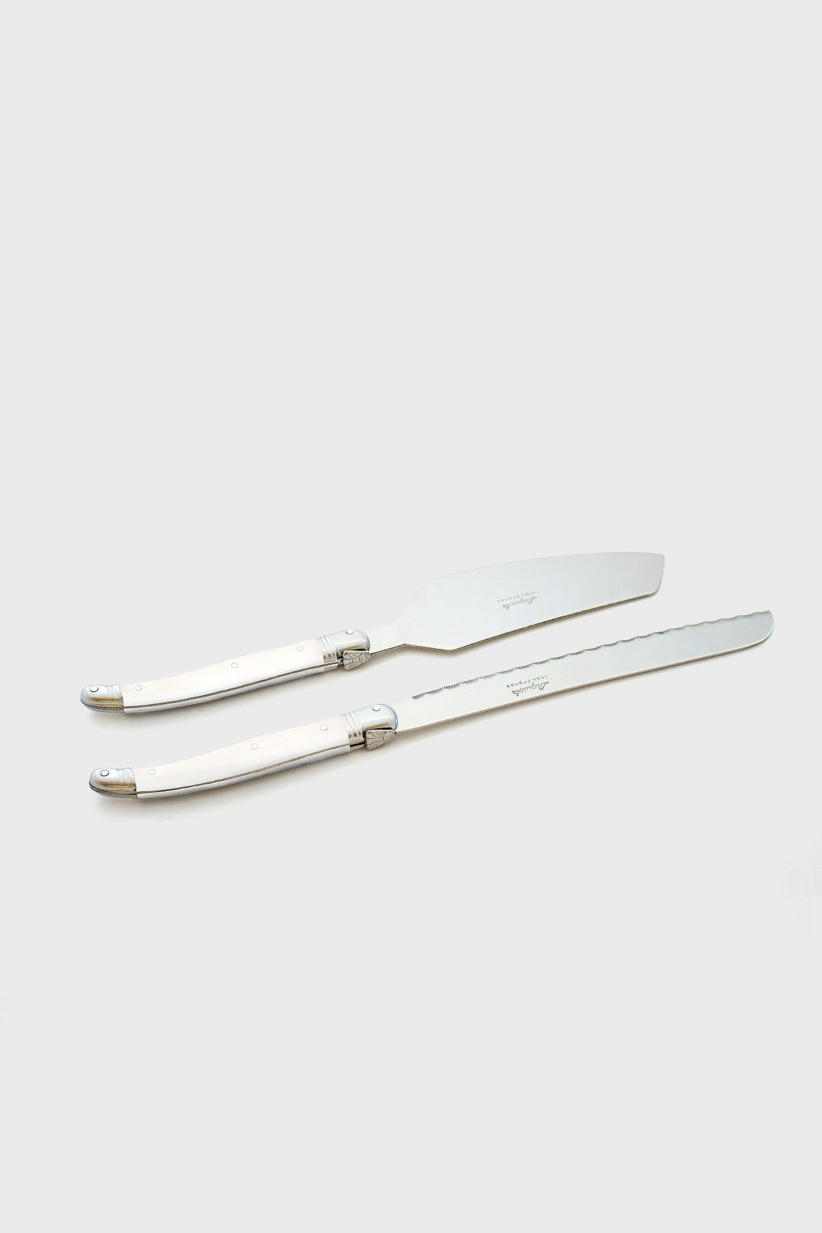 Two stainless steel cake knives with silver handles are placed parallel to each other, reflecting the elegant design of Laguiole flatware.