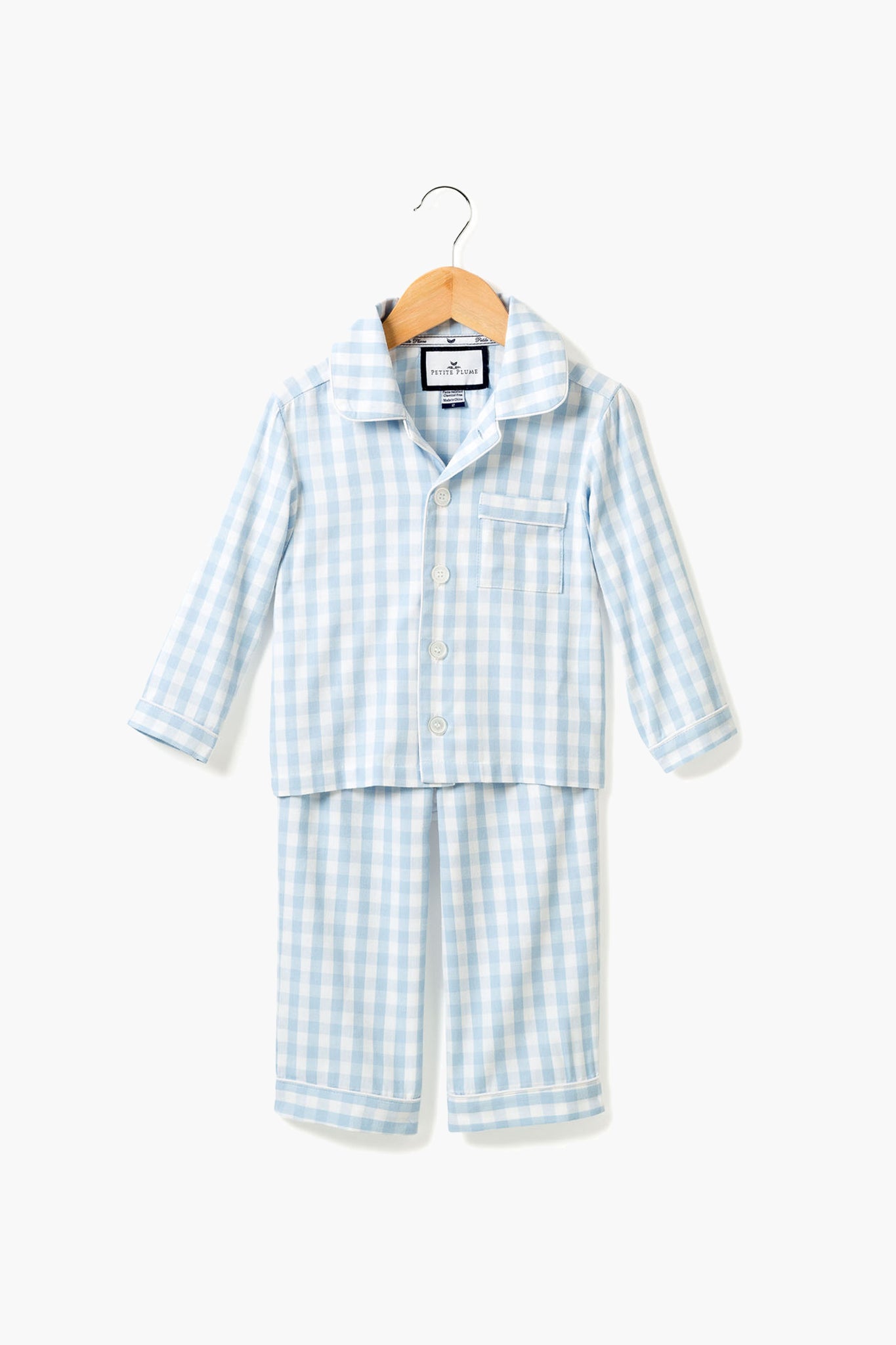 The Petite Plume Light Blue Gingham Pajama Set for children features a button-up long-sleeve top and matching pants in luxury cotton. Elegant family sleepwear, displayed neatly on a hanger.