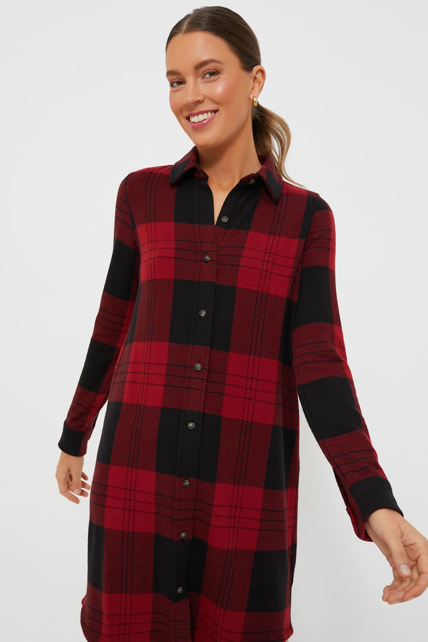 A woman smiles and poses confidently in a Faherty red and black flannel dress made from recycled polyester.