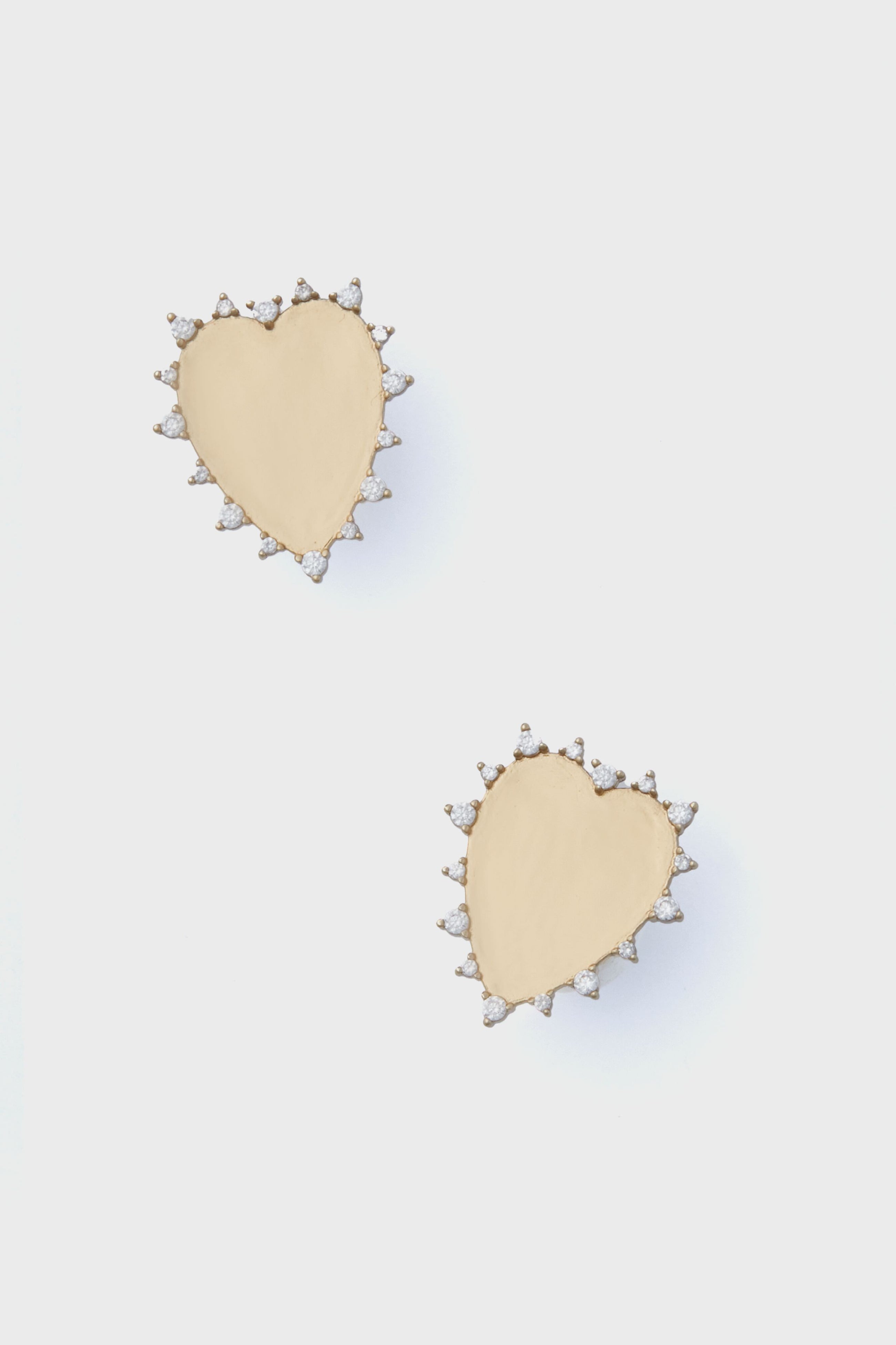 A pair of gold heart stud earrings by Mignonne Gavigan, featuring small clear gemstones outlining each heart and inspired by the brand’s signature crystal studs.