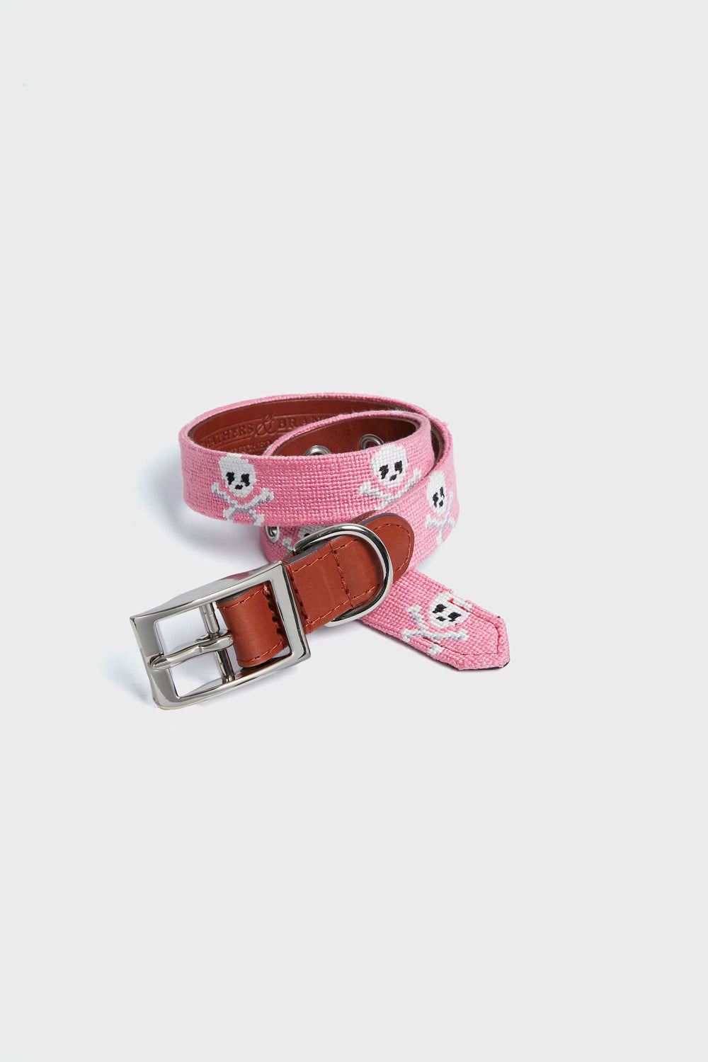 A Smathers and Branson pink needlepoint dog collar features white skull patterns, brown leather accents, and a silver buckle.