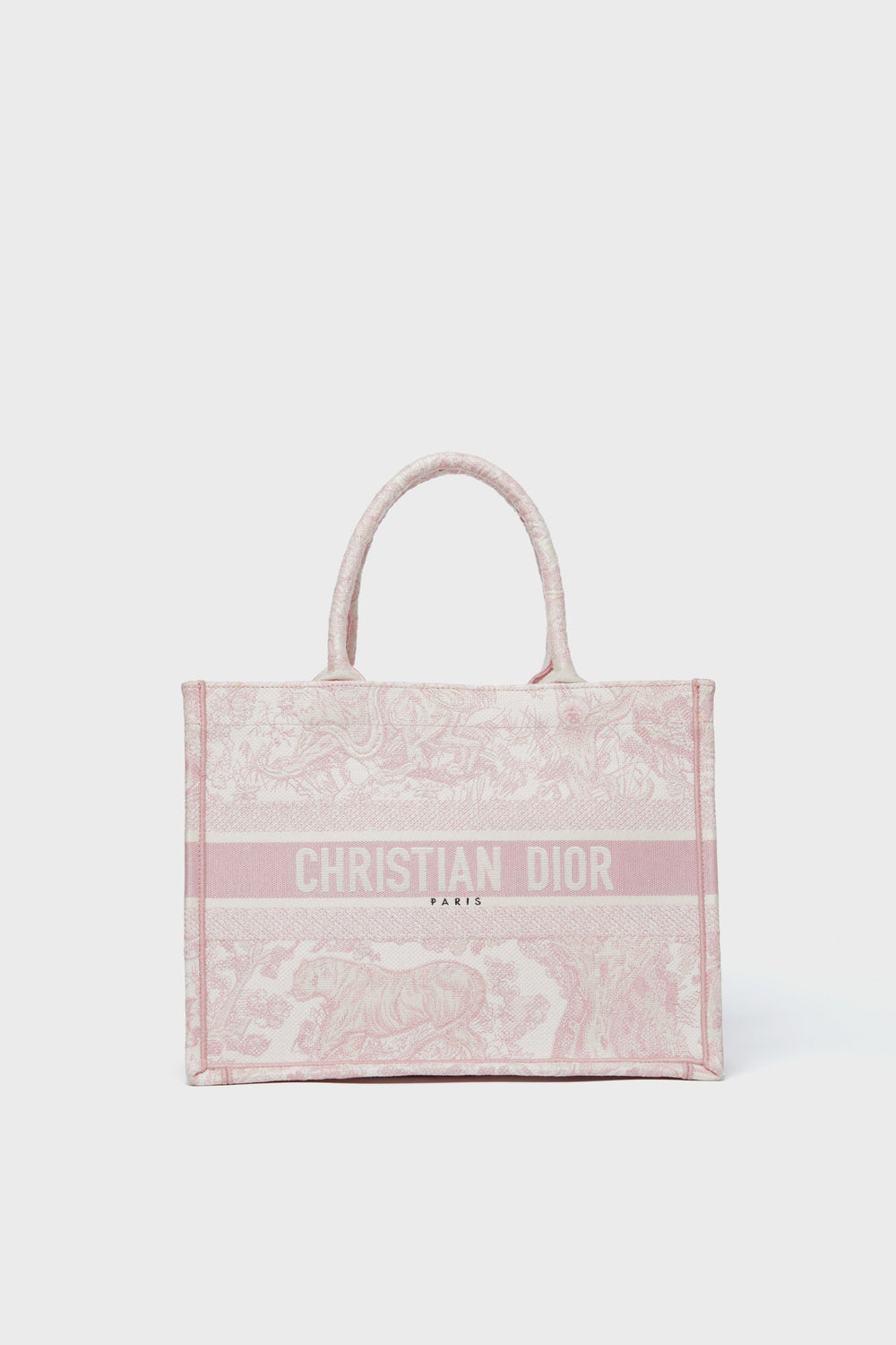A pink Tuckernuck Archive Collection Book Tote with top handles, featuring the brand’s logo and a toile de Jouy pattern embroidered on the front.