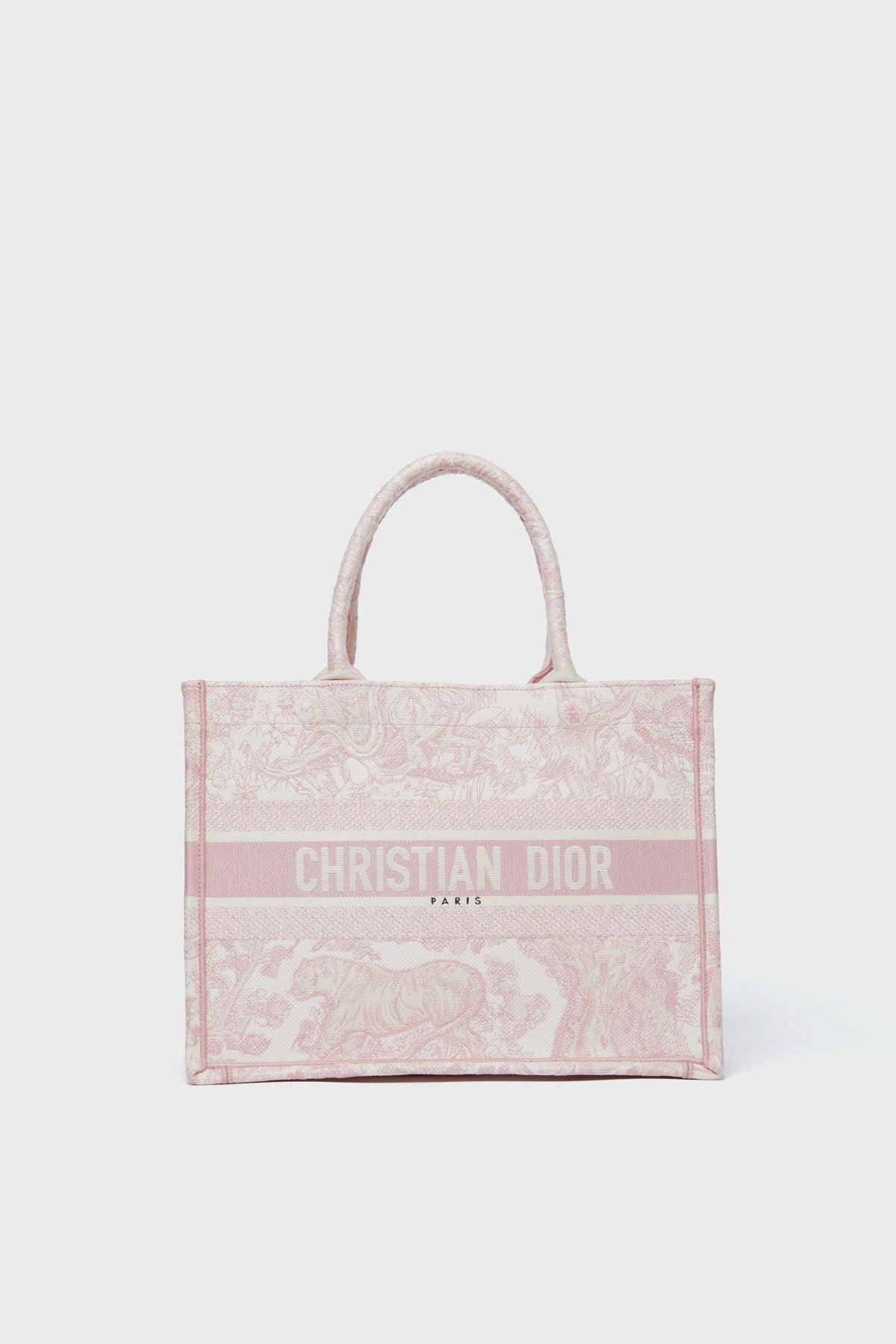 A pink Tuckernuck Archive Collection Book Tote with top handles, featuring the brand’s logo and a toile de Jouy pattern embroidered on the front.