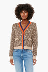 A woman effortlessly showcases the KULE Leopard Milo Cardigan with orange and navy trim, paired with blue jeans and layered gold necklaces, making it a standout statement piece.