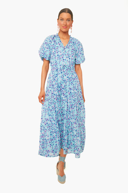 A woman wears a light blue, ankle-length floral dress with short puff sleeves by Banjanan, paired with blue platform sandals.