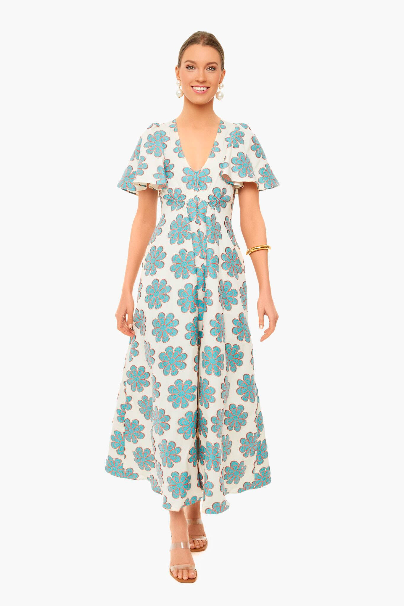 Woman wears a La DoubleJ vintage-inspired white maxi dress with blue floral patterns, short flutter sleeves, and a v-neckline. She styles it with strappy sandals and simple jewelry for effortless elegance.