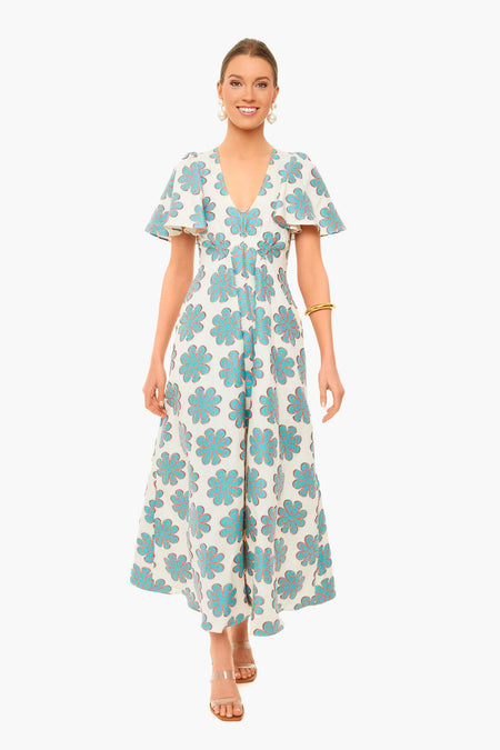 Woman wears a La DoubleJ vintage-inspired white maxi dress with blue floral patterns, short flutter sleeves, and a v-neckline. She styles it with strappy sandals and simple jewelry for effortless elegance.