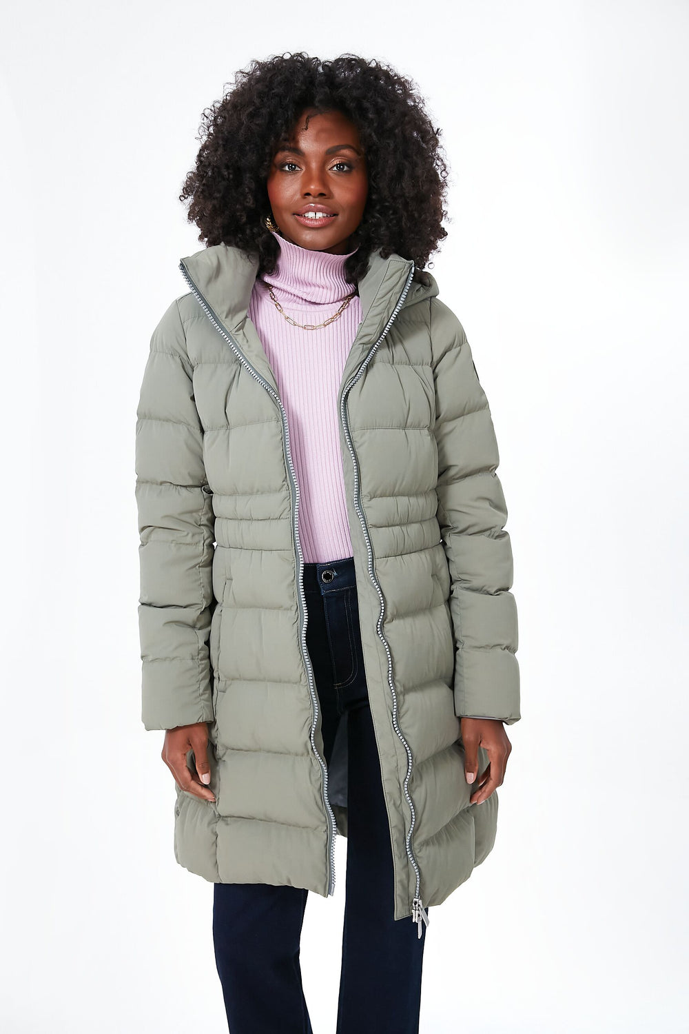 A woman models a Canada Goose light green Aurora Parka over a light pink turtleneck sweater and dark pants, highlighting the warmth of duck down.