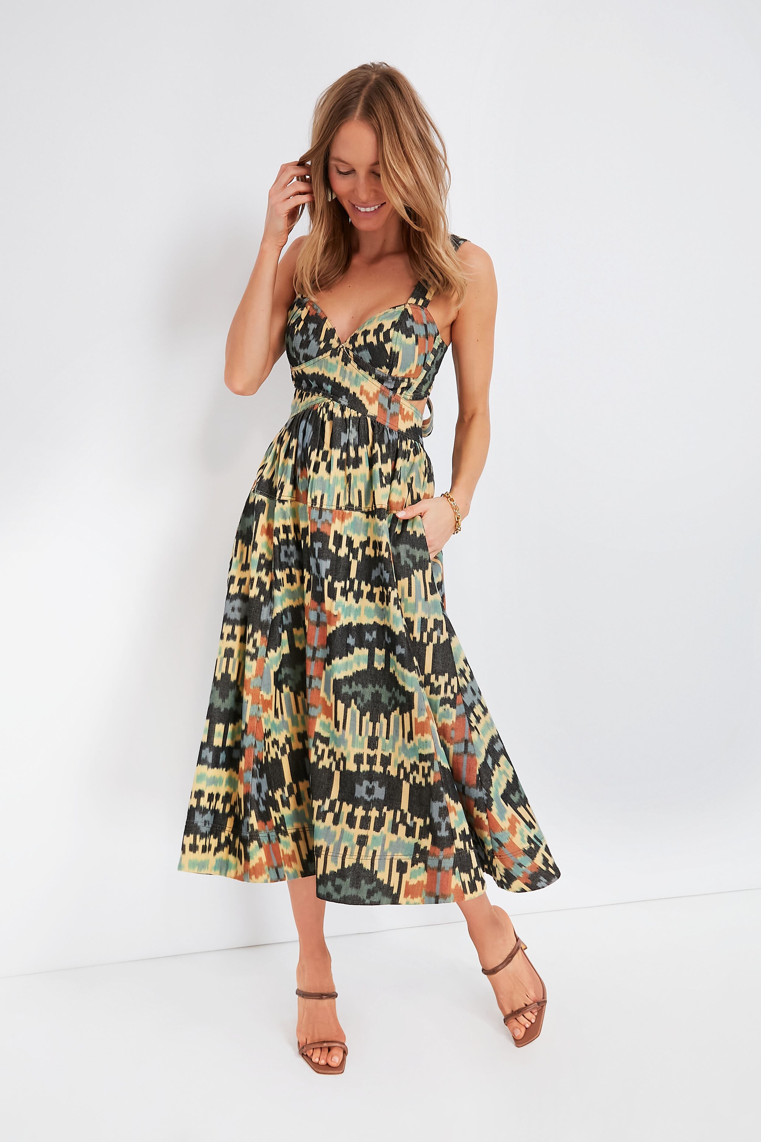 A woman smiles and touches her hair while wearing a sleeveless Ulla Johnson dress with thin straps, paired with strappy sandals.
