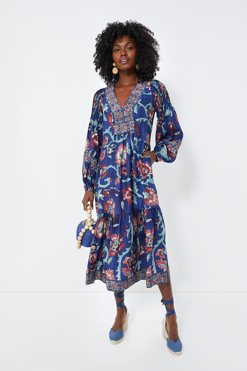 A woman in a Sea New York Rory Print Dress with long sleeves and a V-neckline, carrying a small blue bag and wearing blue ankle-tie espadrilles.