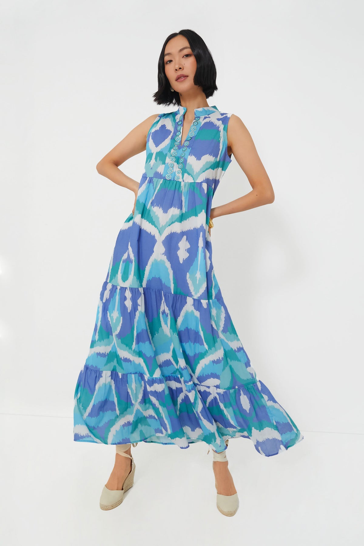 A woman wears the Sheridan French Cerulean Watercolor Ikat Tessa Dress, a sleeveless, long, tiered maxi featuring handmade prints in blue, turquoise, and white.