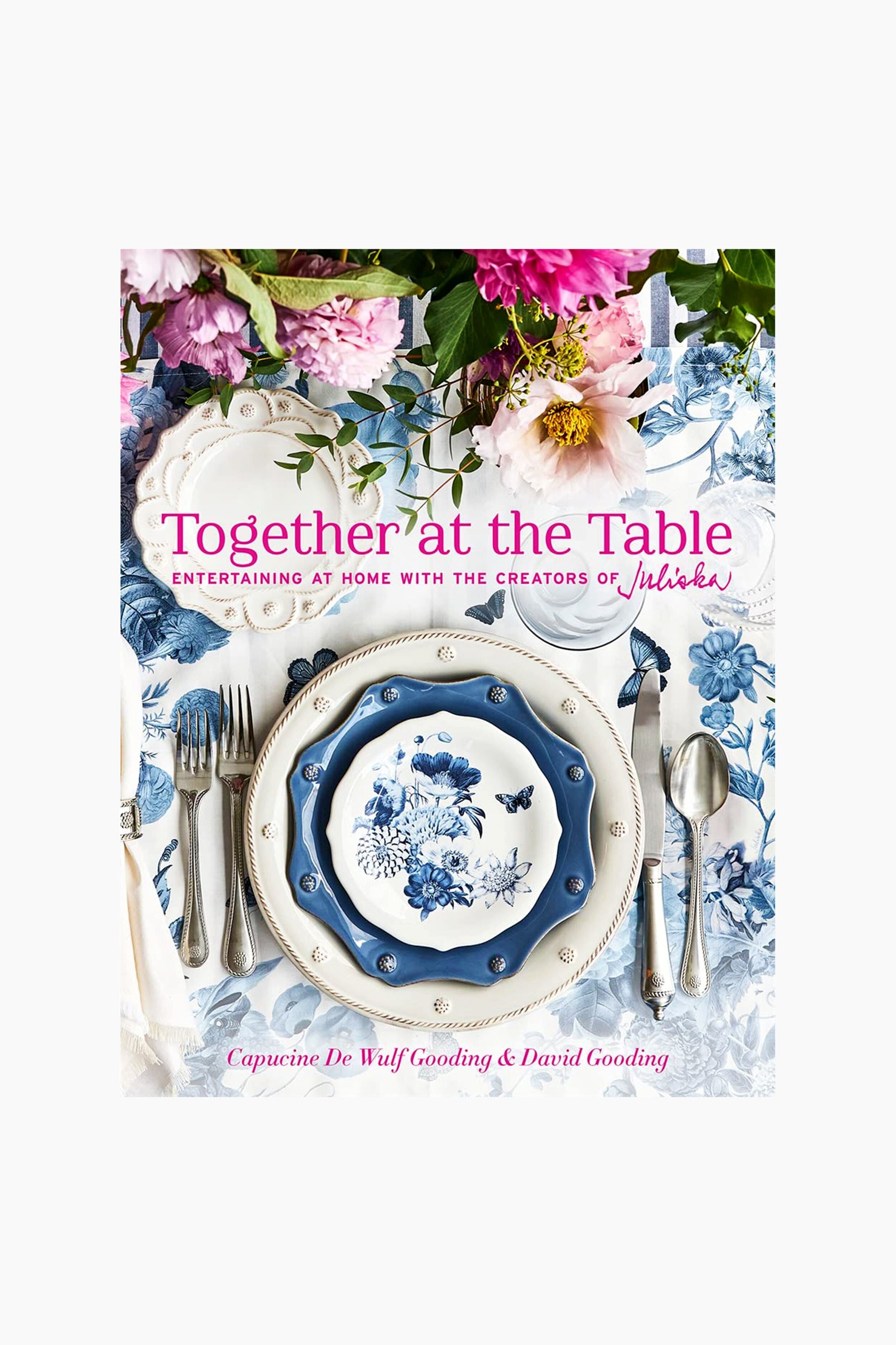 A blue and white floral table setting with Juliska plates, cutlery, Bohemian glassware, pink flowers, and the book "Together at the Table" by Capucine De Wulf Gooding & David Gooding—perfect for entertaining.