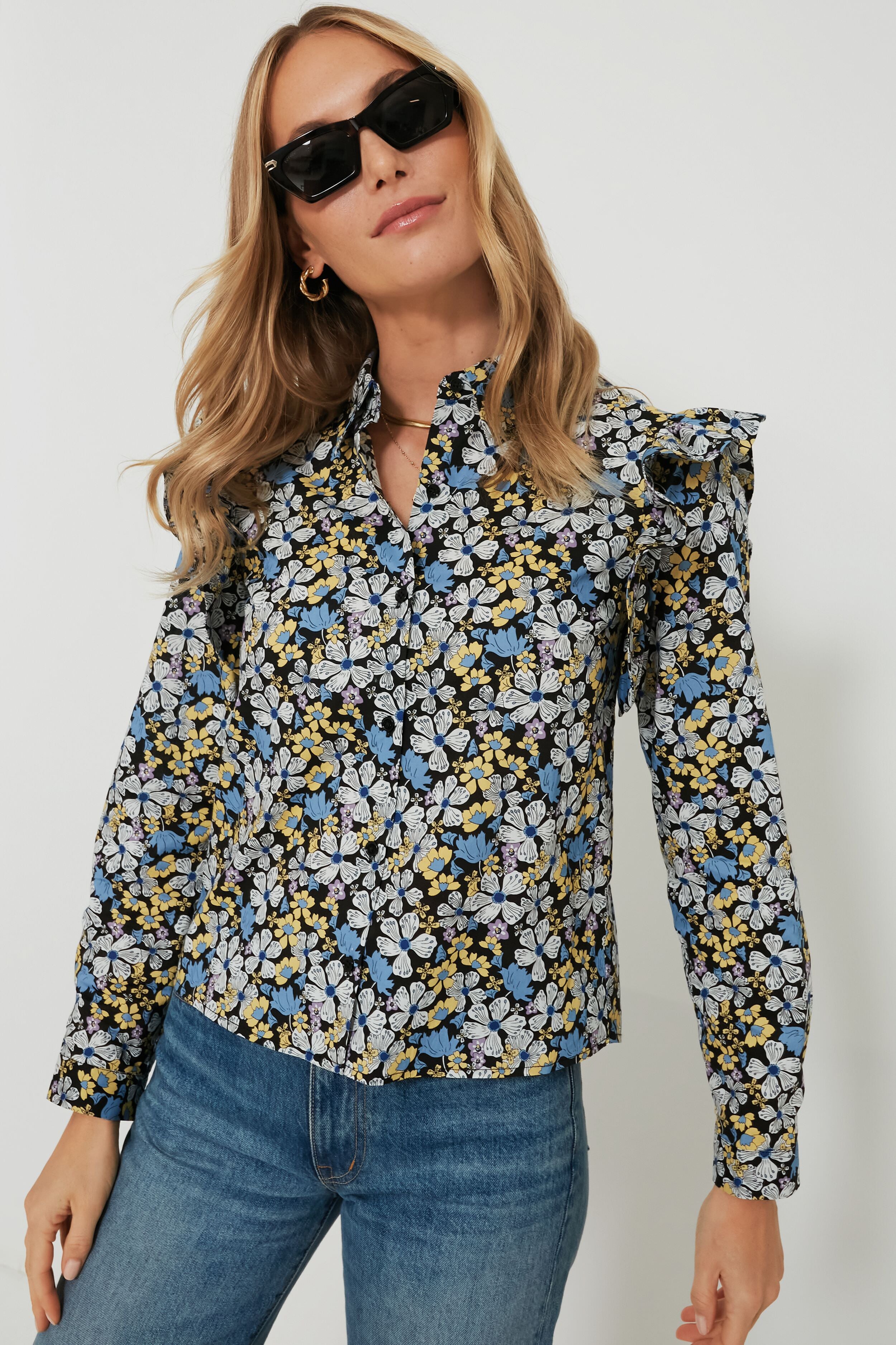 A woman stands confidently, wearing Hyacinth House sunglasses and a long-sleeve floral blouse with ruffle details, paired with blue jeans.