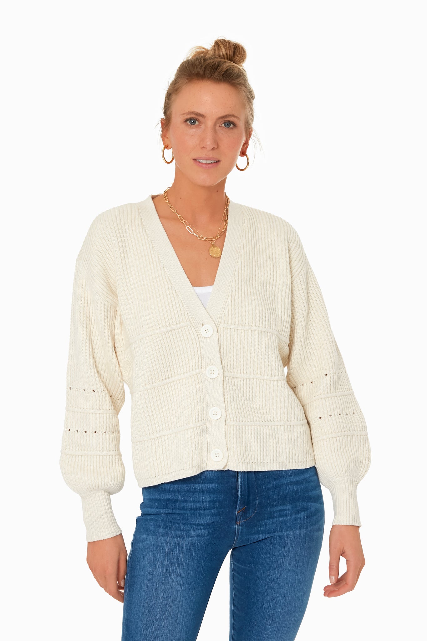 A woman showcases classic style in an Apiece Apart white knit cardigan, paired with a white top and blue jeans.