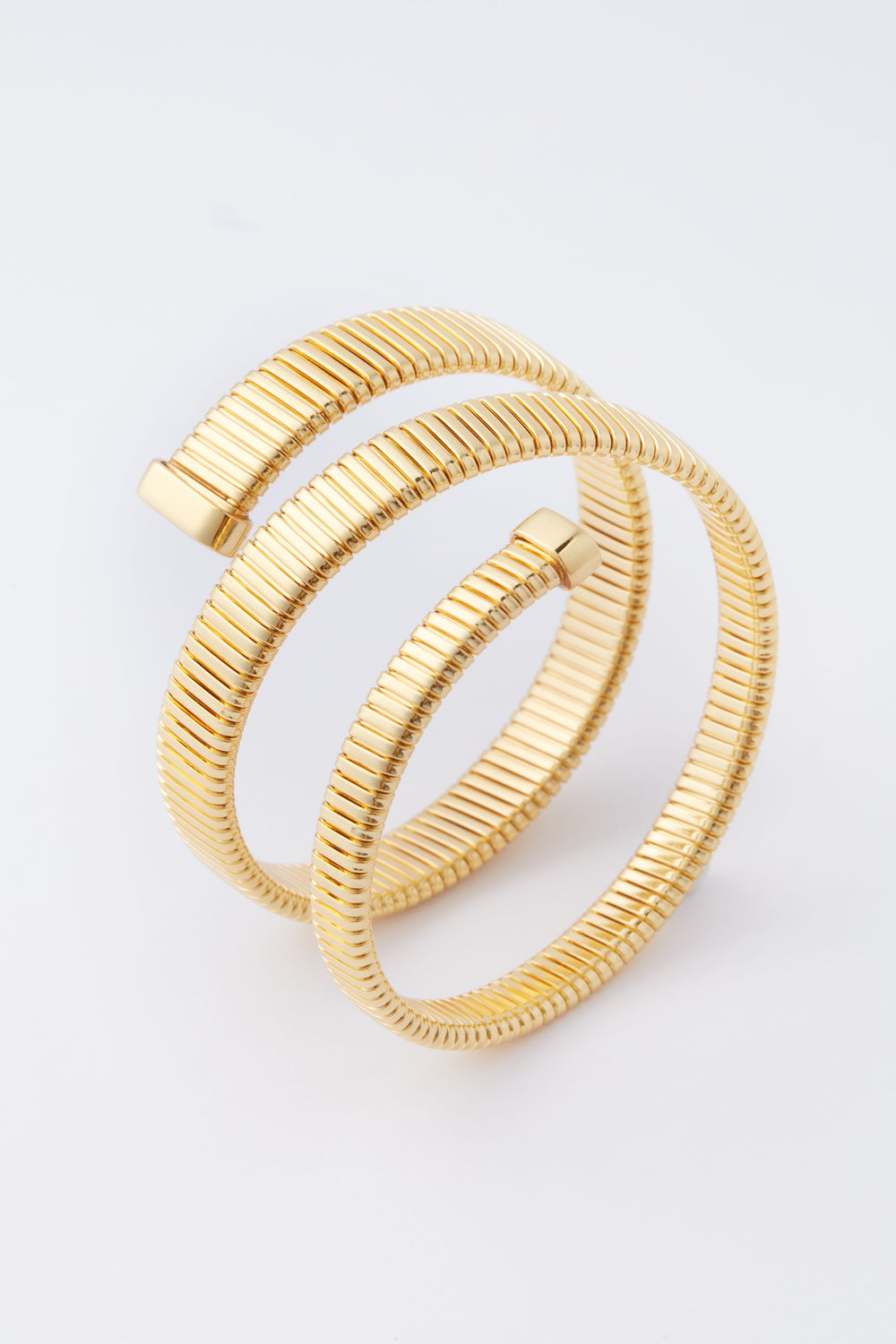 A gold-plated, coiled serpent chain bracelet with ribbed texture and two open ends by Tuckernuck Jewelry—a stunning statement piece.