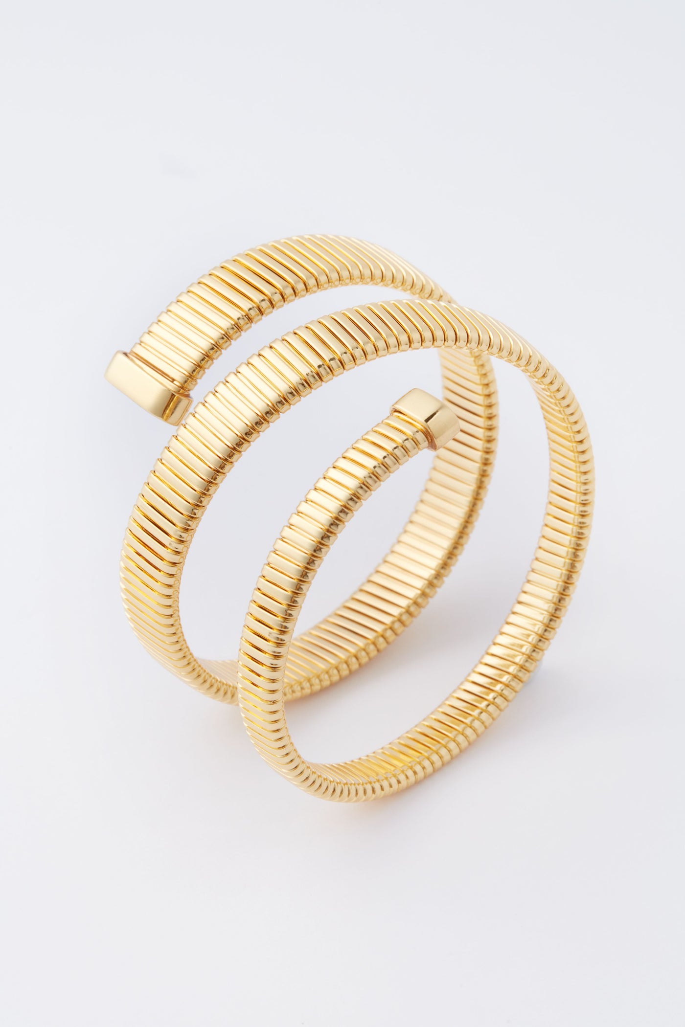 A gold-plated, coiled serpent chain bracelet with ribbed texture and two open ends by Tuckernuck Jewelry—a stunning statement piece.