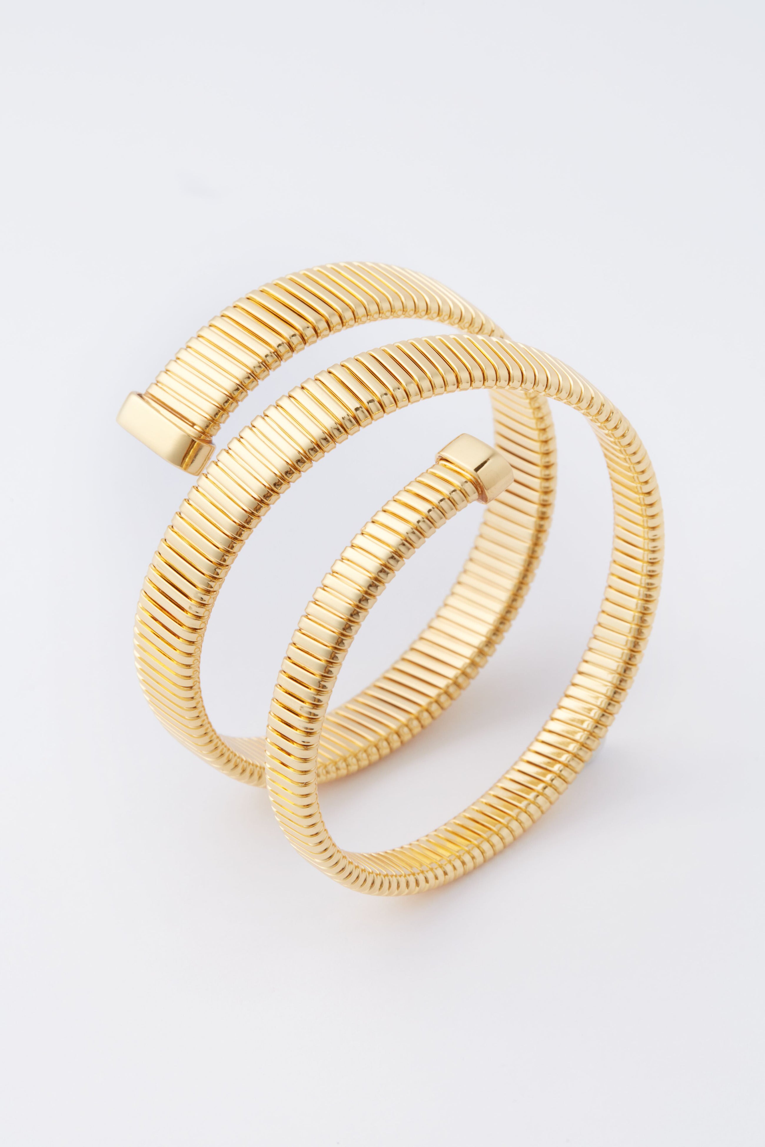 A gold-plated, coiled serpent chain bracelet with ribbed texture and two open ends by Tuckernuck Jewelry—a stunning statement piece.