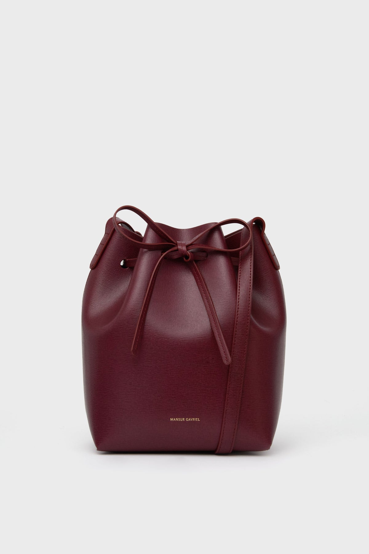 The Mansur Gavriel burgundy mini bucket bag is crafted from Italian calf leather, featuring a drawstring closure and a shoulder strap.