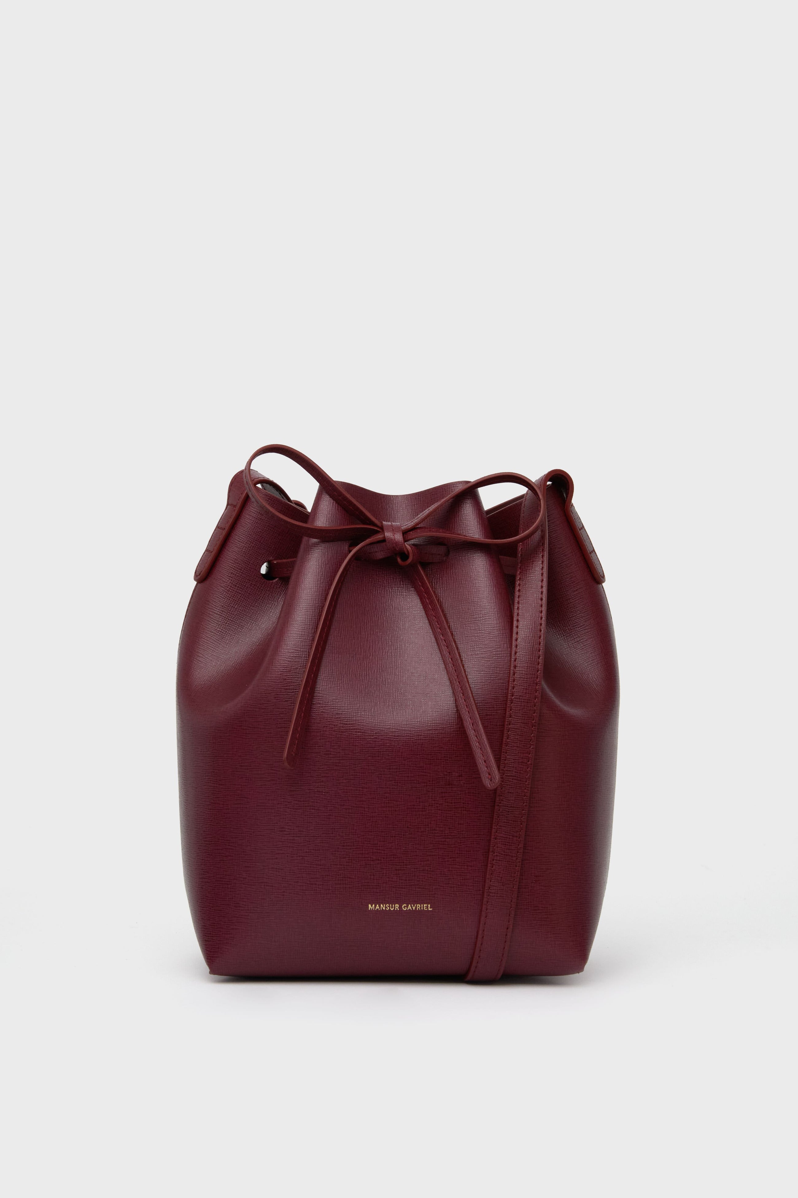The Mansur Gavriel burgundy mini bucket bag is crafted from Italian calf leather, featuring a drawstring closure and a shoulder strap.