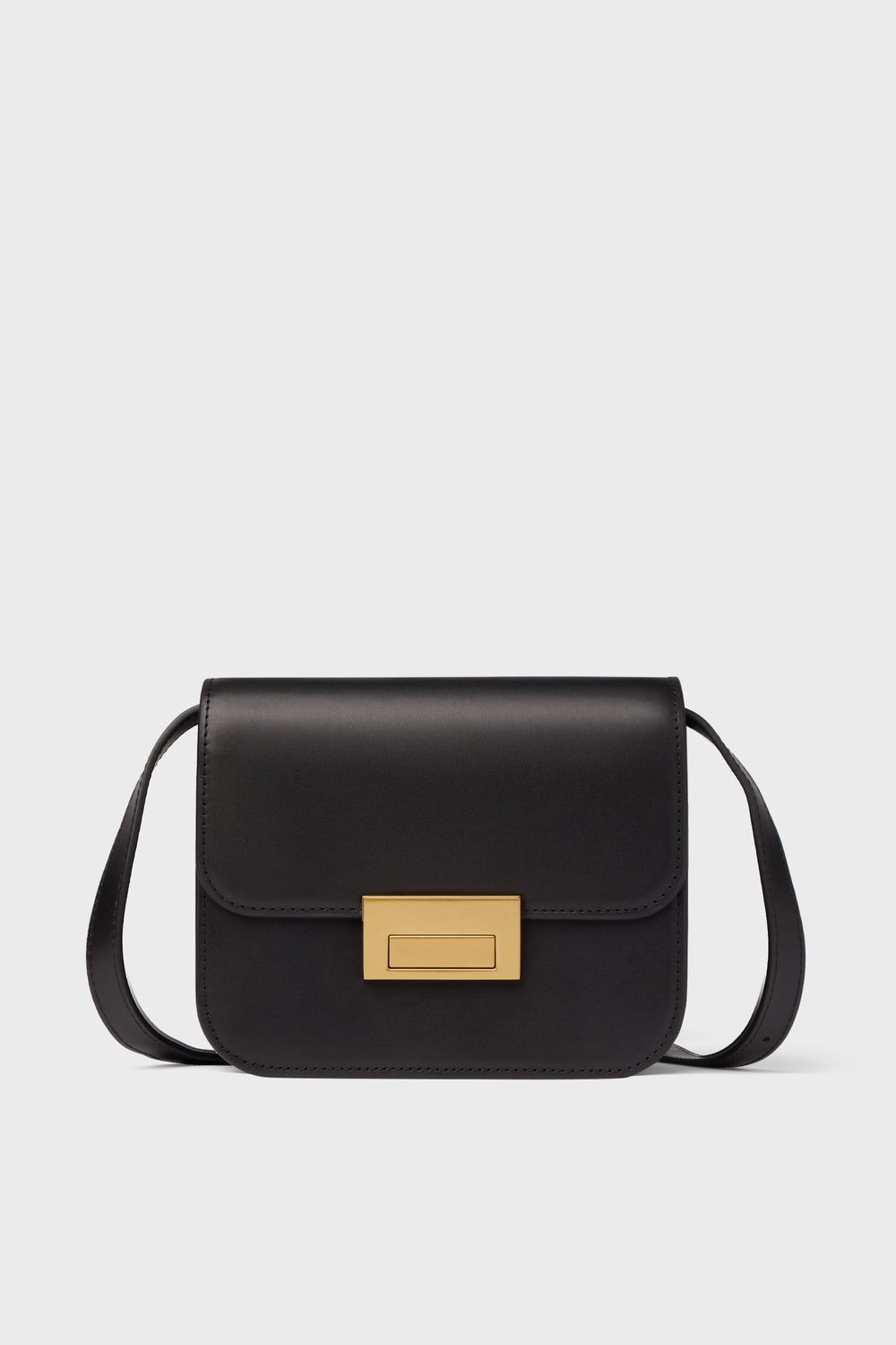A Loeffler Randall black crossbody bag in Italian vachetta leather features a rectangular gold clasp and a long strap.