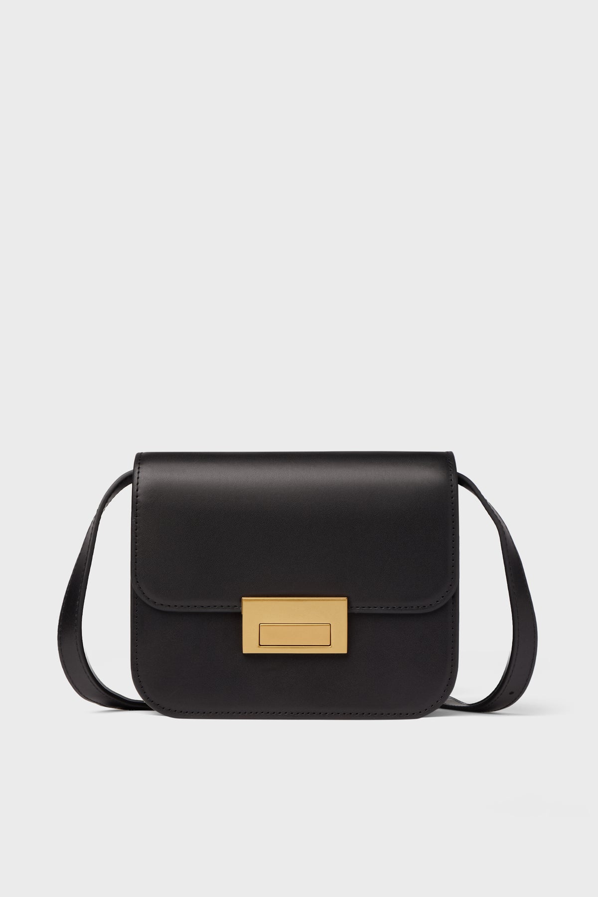 A Loeffler Randall black crossbody bag in Italian vachetta leather features a rectangular gold clasp and a long strap.