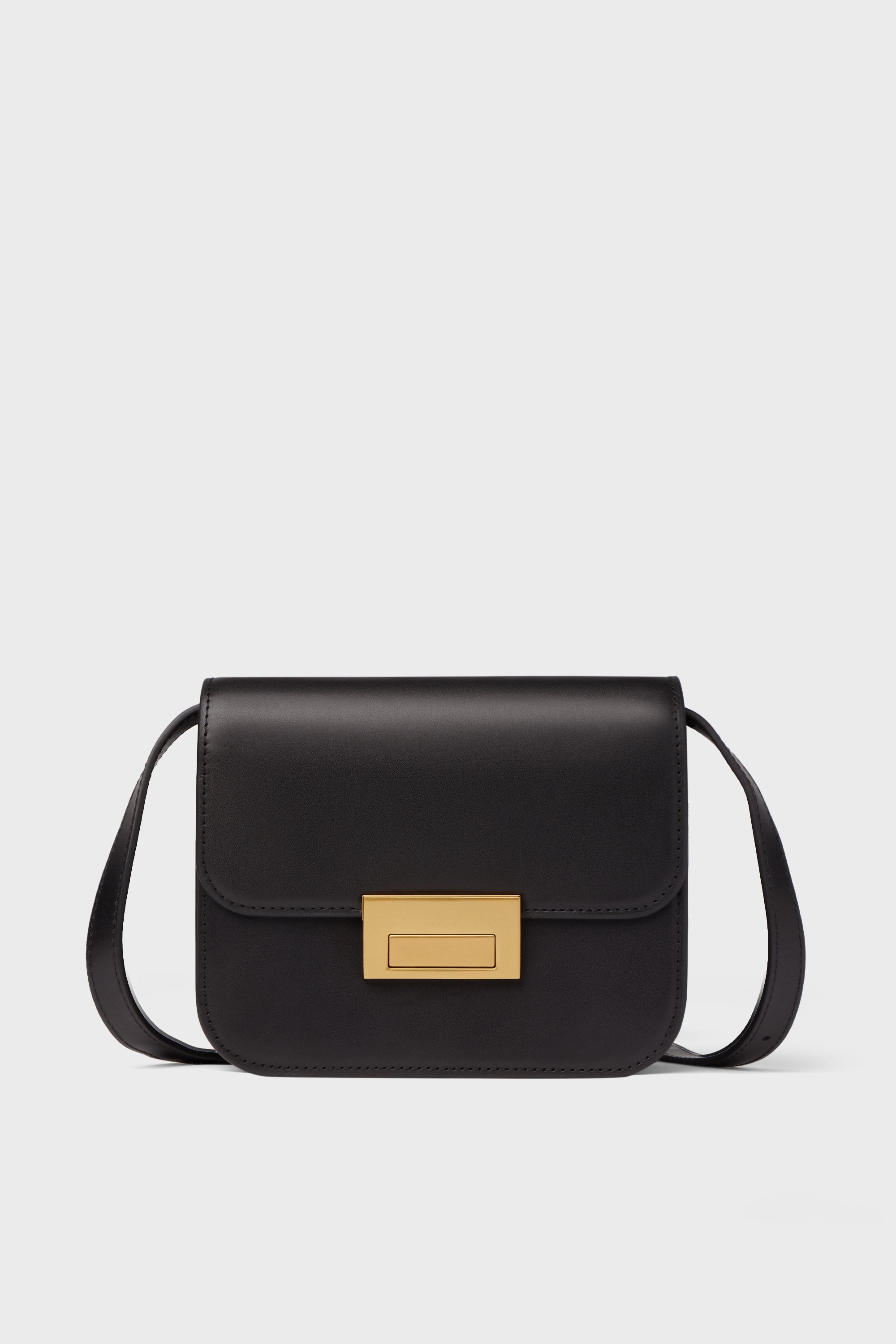 A Loeffler Randall black crossbody bag in Italian vachetta leather features a rectangular gold clasp and a long strap.