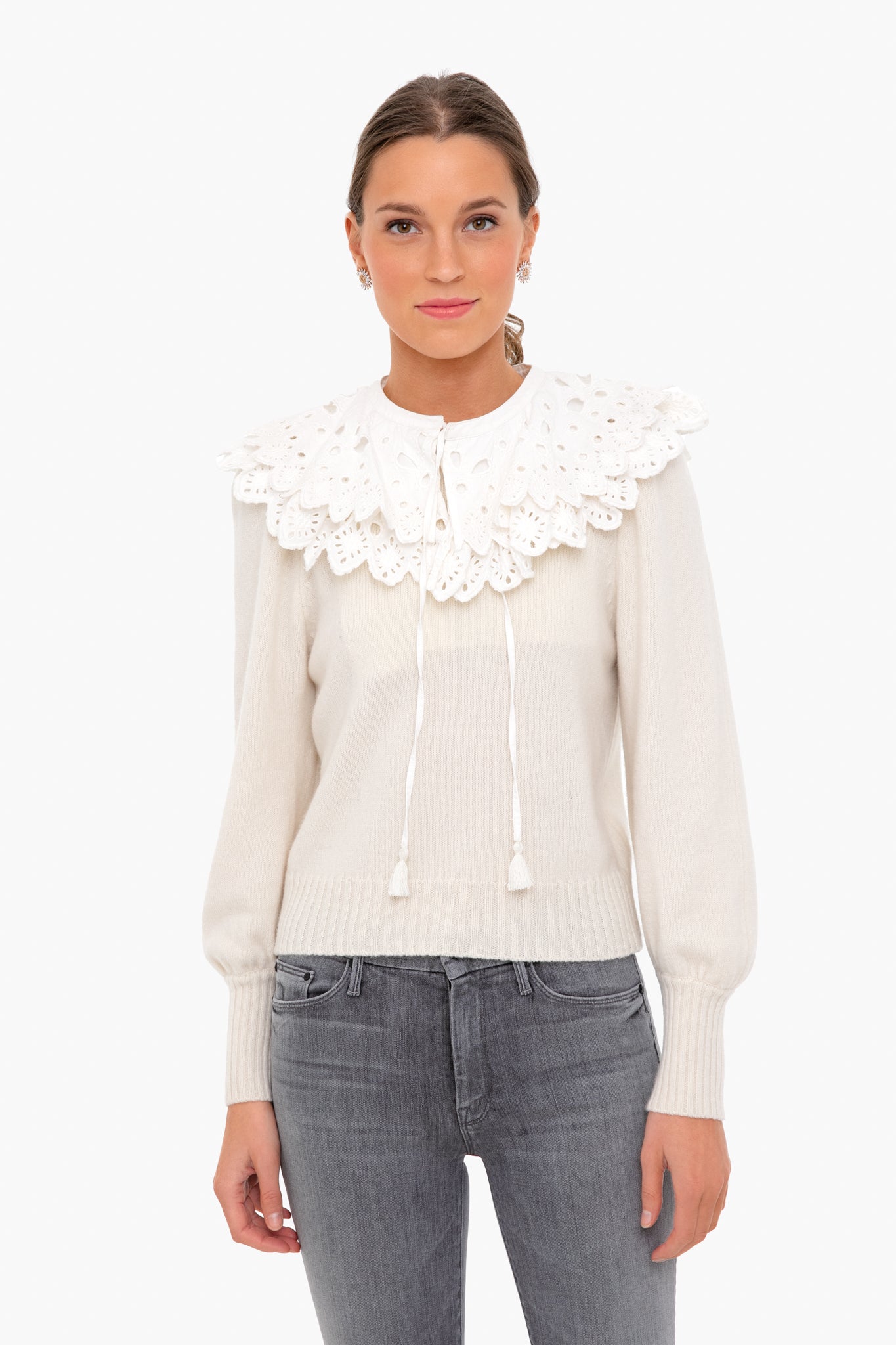A woman wears a cream eyelet lace sweater with a large, layered collar from Sea New York, paired with light gray jeans.