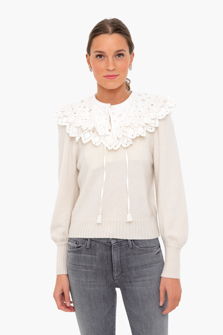 A woman wears a cream eyelet lace sweater with a large, layered collar from Sea New York, paired with light gray jeans.