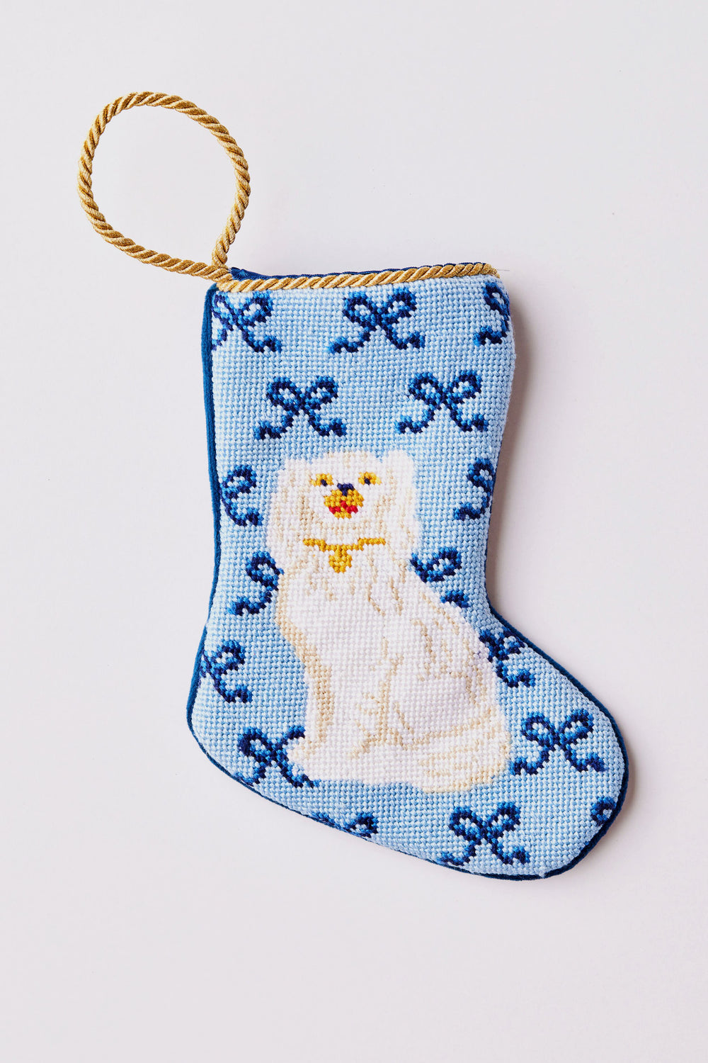 A small blue hand-stitched Christmas stocking by Bauble Stockings, with a gold loop and needlepoint design of a white dog amid blue patterns—a charming, fair trade gift.