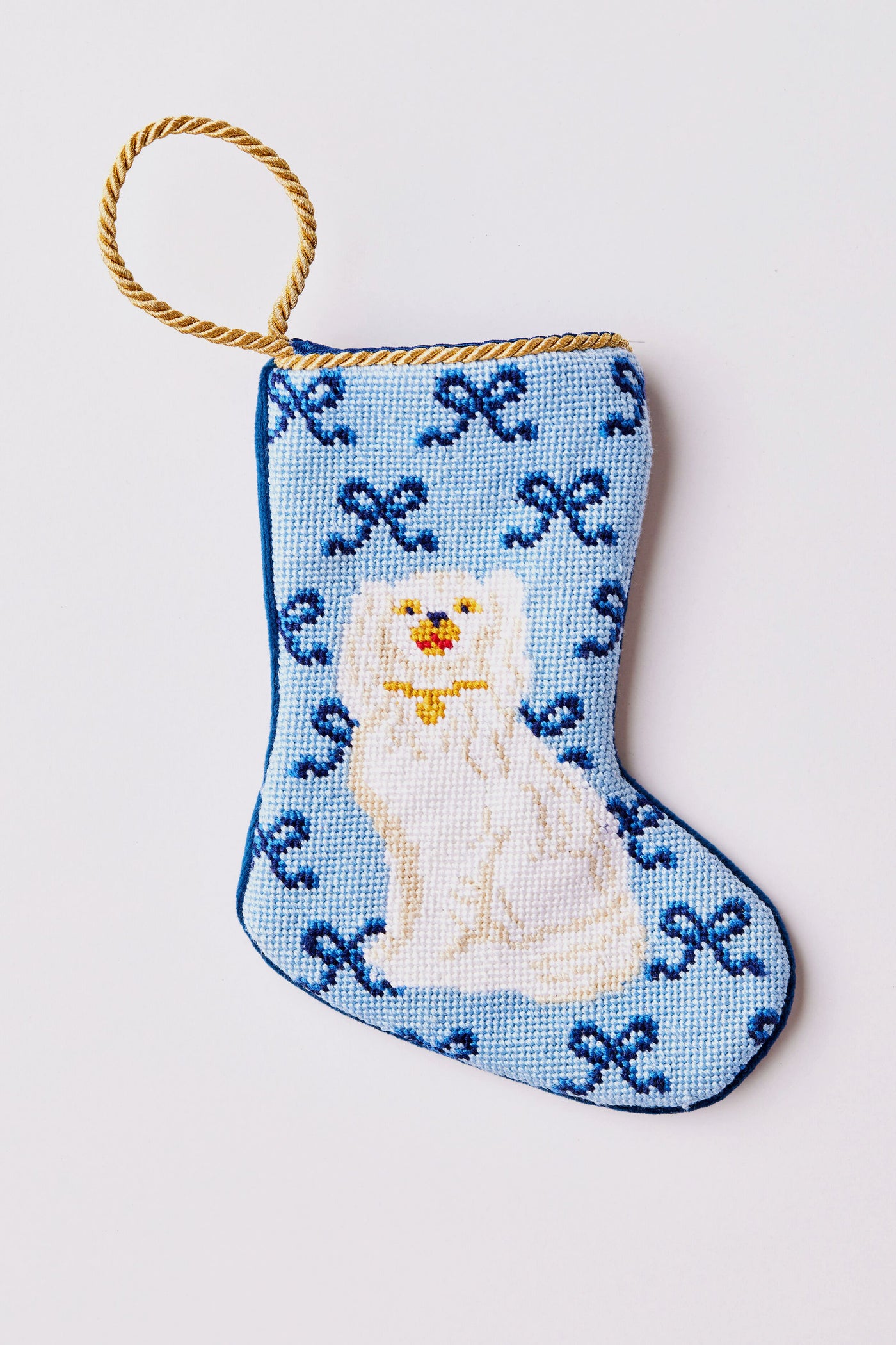 A small blue hand-stitched Christmas stocking by Bauble Stockings, with a gold loop and needlepoint design of a white dog amid blue patterns—a charming, fair trade gift.