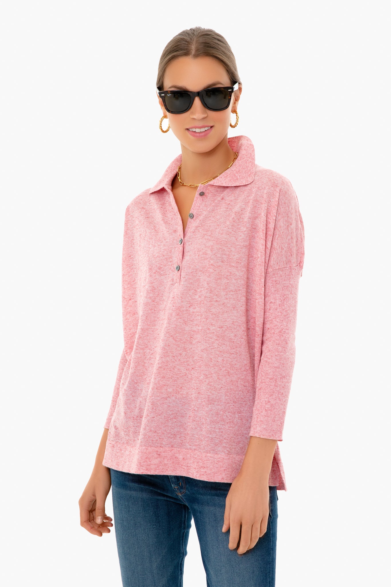 A woman in a Tuckernuck light pink collared long-sleeve shirt, blue jeans, black sunglasses, hoop earrings, and a gold necklace.