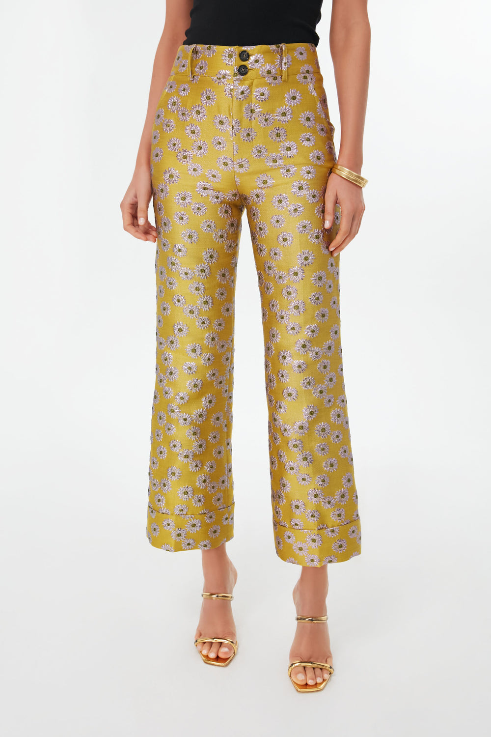 A person wears La DoubleJ yellow high-waisted floral flare pants, a black top, gold sandals, and gold bangles.