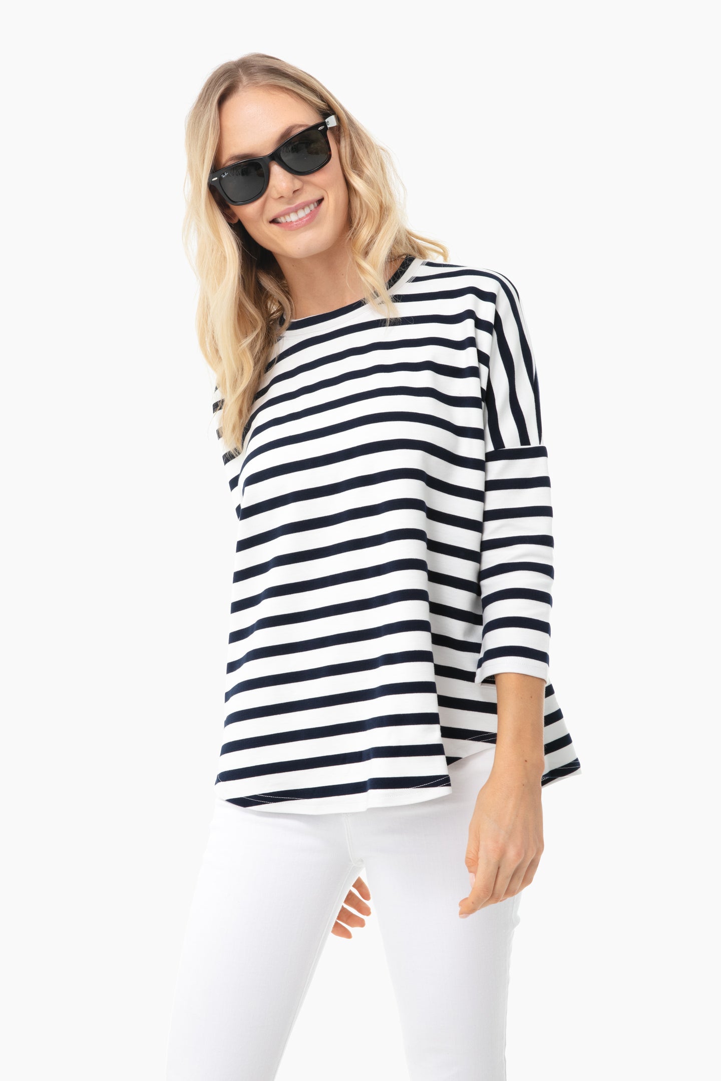 A woman models a Pomander Place sweatshirt—versatile for travel—styled with sunglasses, a black and white striped long-sleeve top, and white pants.
