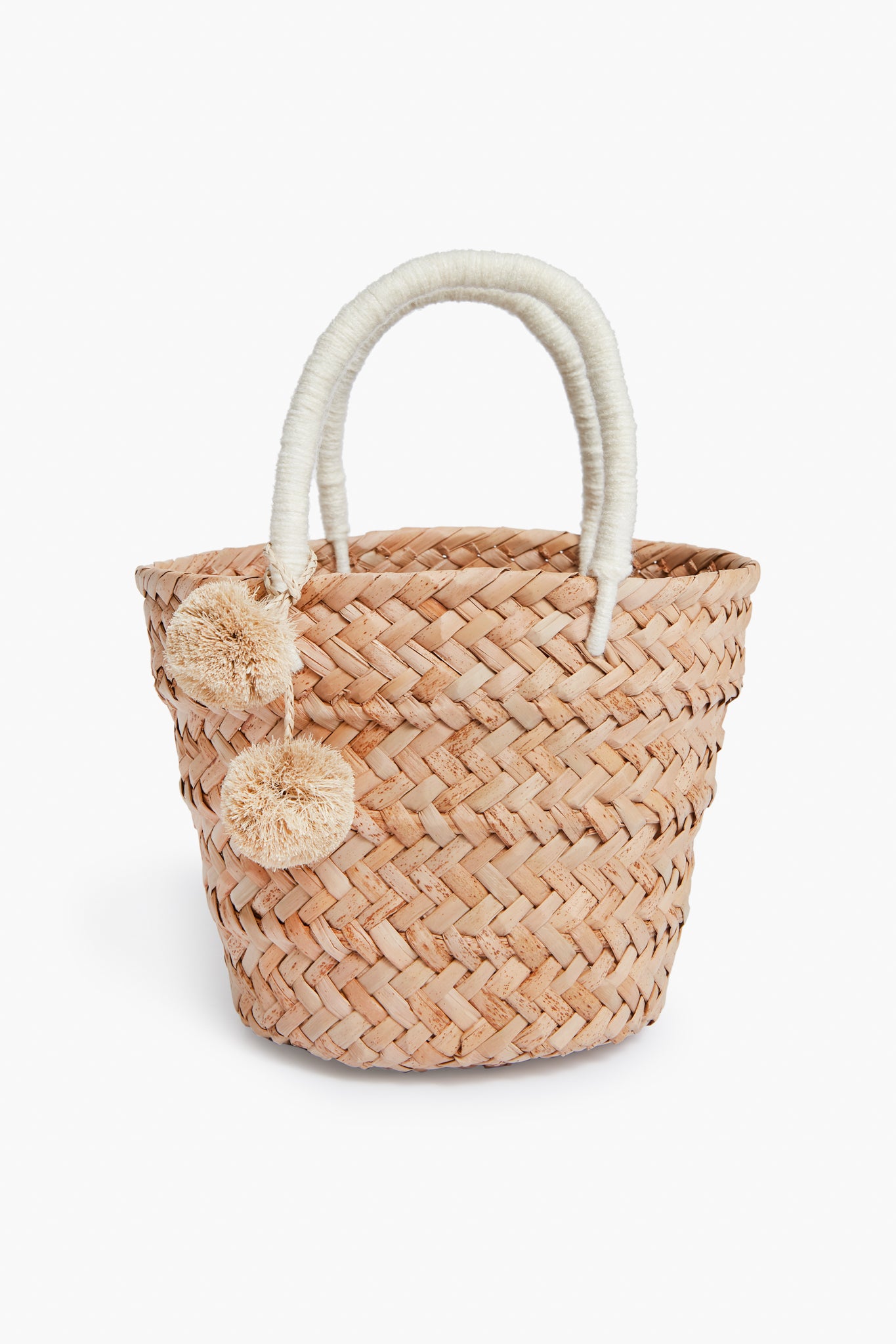 The Kayu woven straw tote bag features two wrapped handles and beige pom-pom accents, expertly crafted with Filipino basket weaving techniques for a timeless, sustainable accessory.