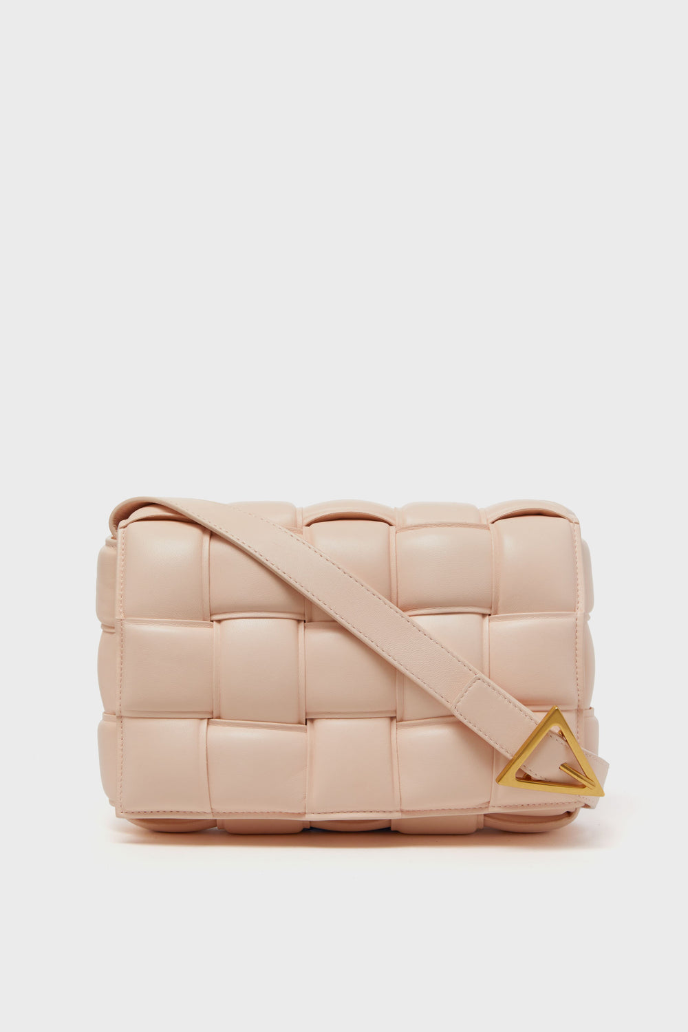 A beige, woven leather Tuckernuck Archive Collection Cassette Bag with a wide strap and gold triangular buckle is shown.